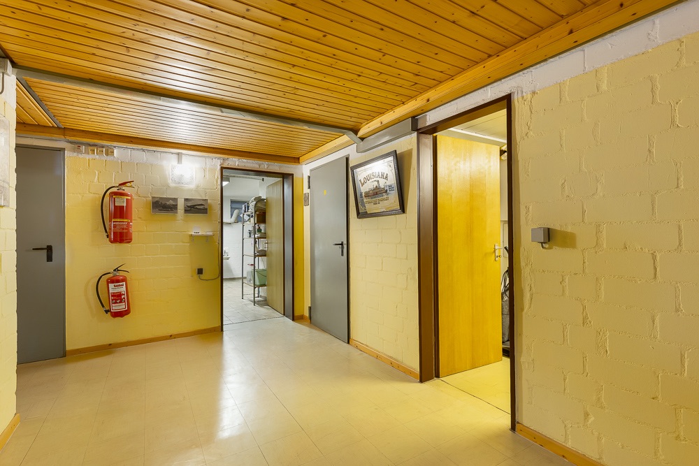 Heller Flur mit Holzboden, Holzbalkendecke, mehreren Türen und zwei Feuerlöschern an der Wand.