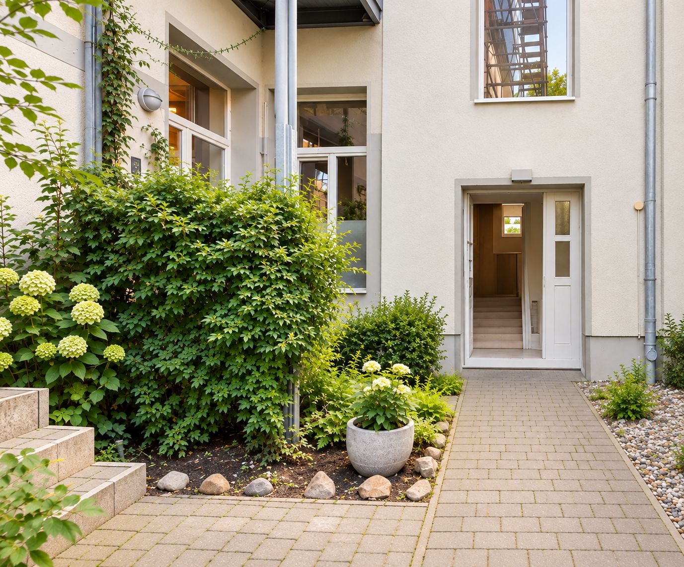 Eingangsbereich eines Wohnhauses mit bepflanztem Vorgarten und Pflasterweg.