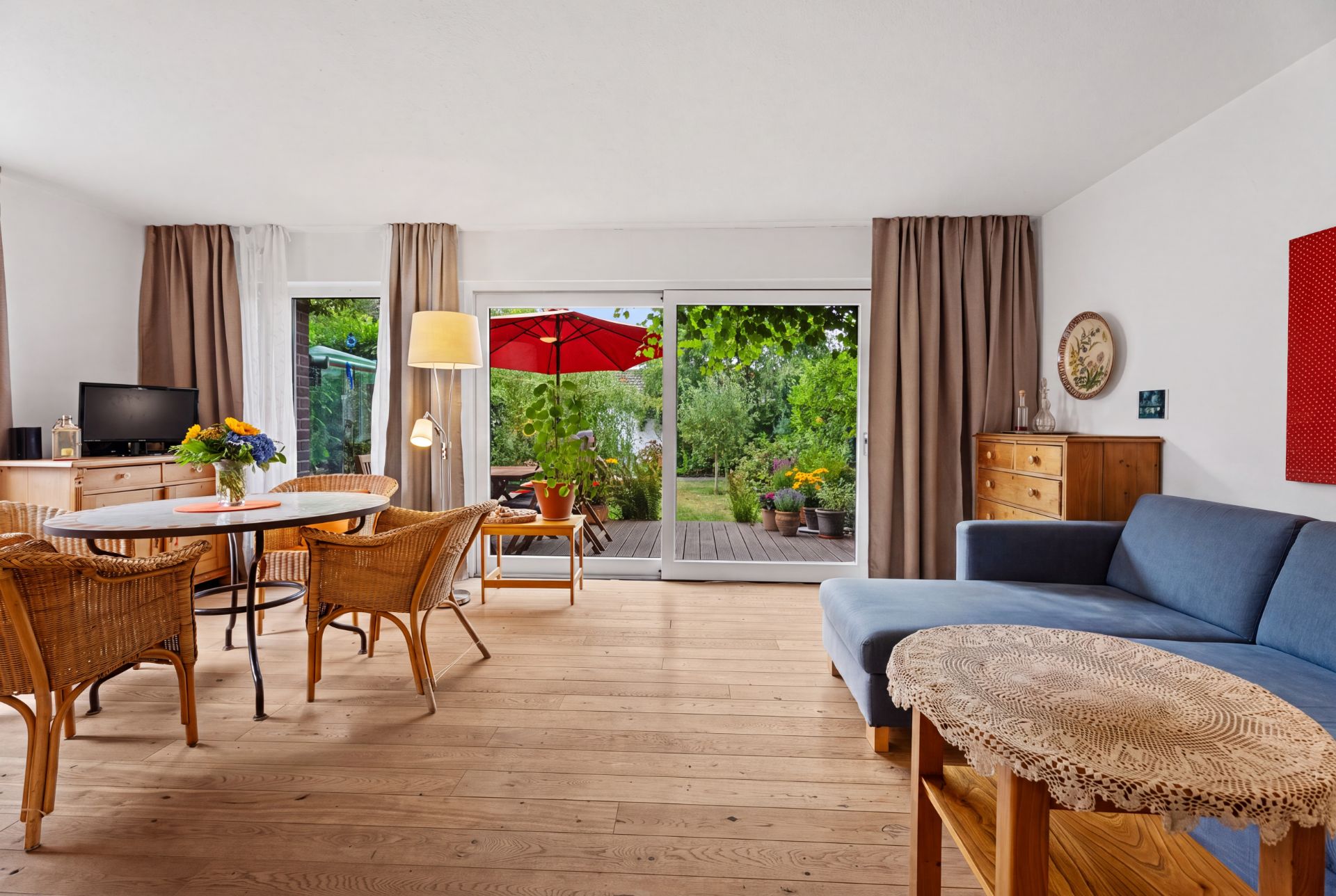 Helles Wohnzimmer mit Holzboden, Essbereich, Sofa und Zugang zu einer Terrasse mit Garten.