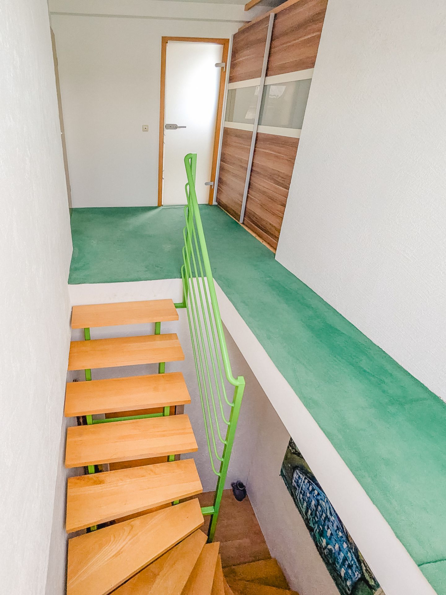 Holztreppe mit grünem Geländer führt zu Flur mit grünem Boden und Schiebetür aus Holz.