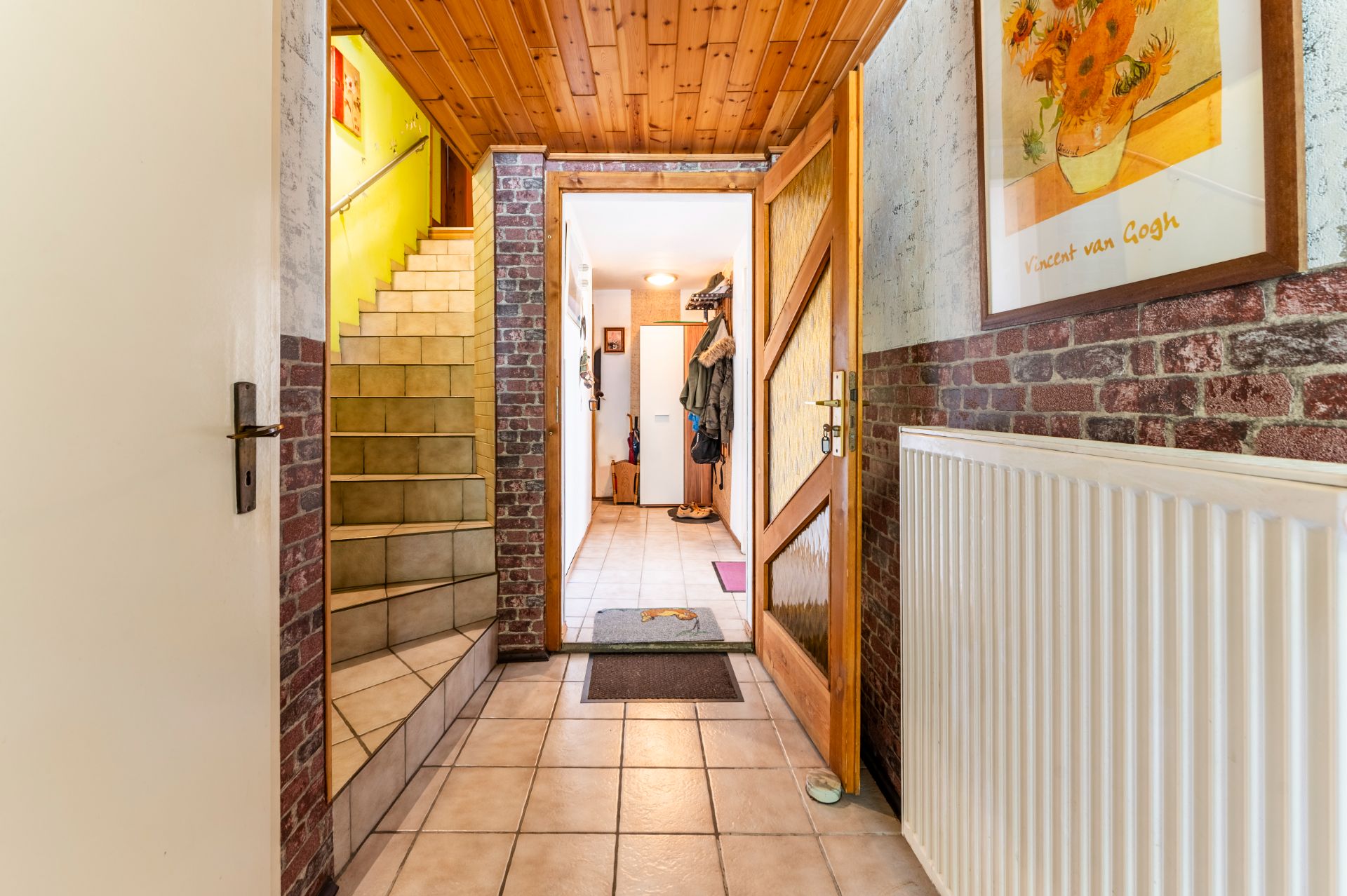 Eingangsbereich mit offener Holztür, Flur, Treppe und Wandbild, Fliesenboden, Holzdecke.