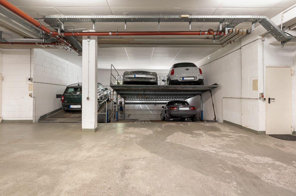 Tiefgaragenstellplätze mit zwei Ebenen und geparkten Autos, weiße Wände und Betondecke.