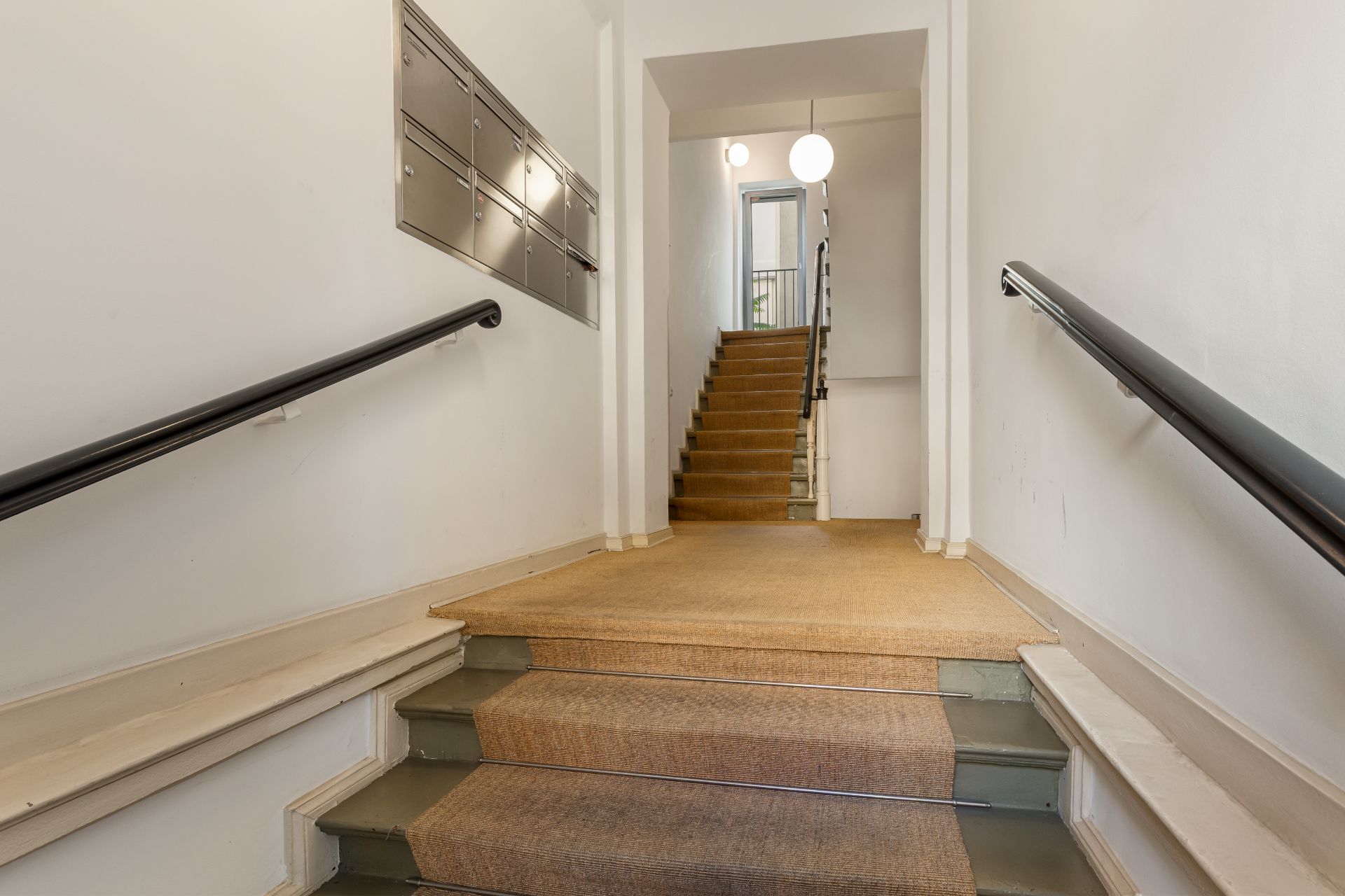 Treppenhaus eines Wohngebäudes mit Handläufen und Briefkästen an der Wand.