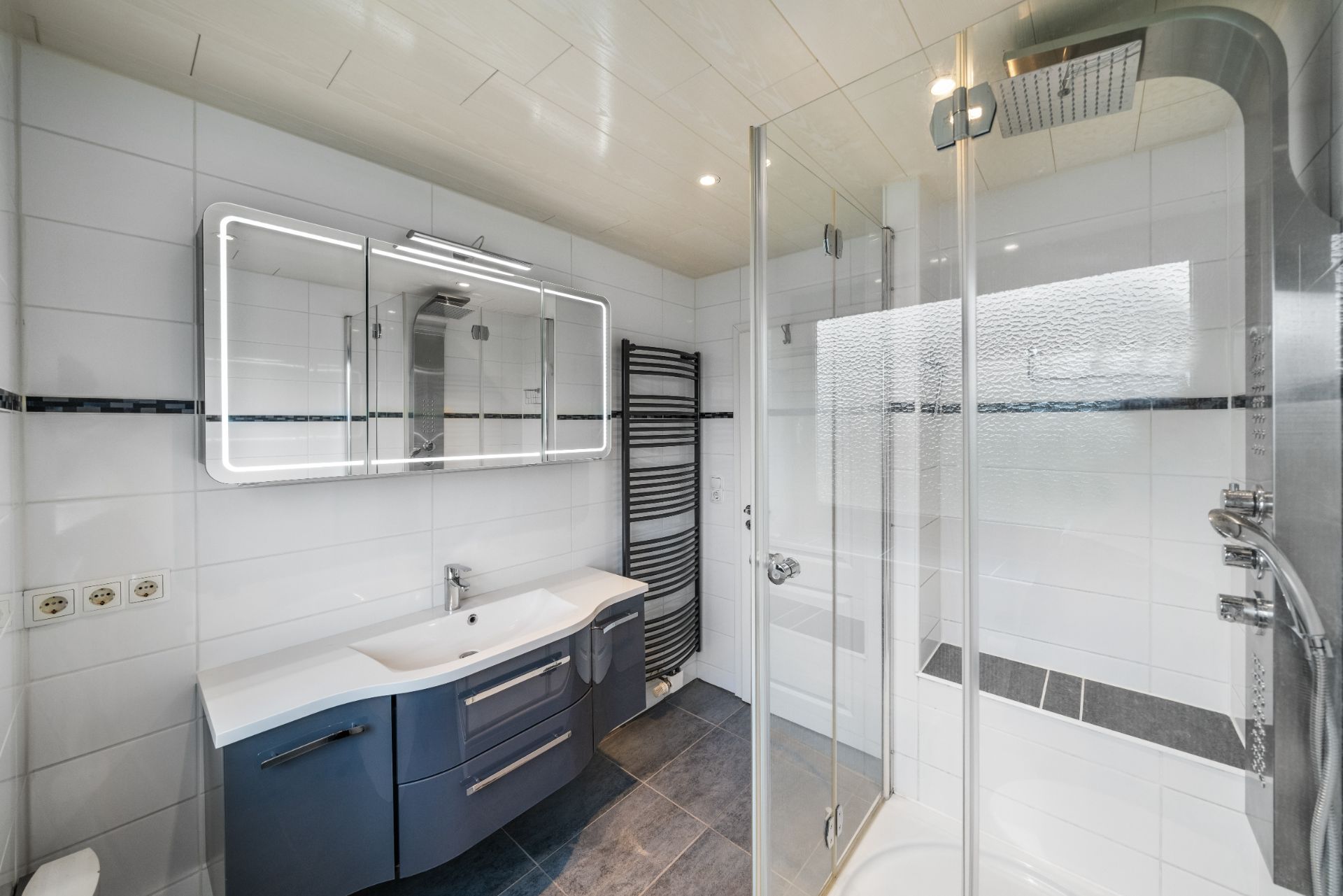 Modernes Bad mit Glasdusche, großem Spiegel, Waschbecken und Handtuchheizkörper.