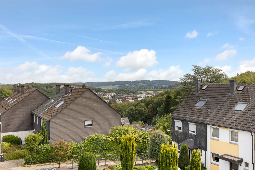 Blick auf Wohnhäuser mit Gärten und Hügel im Hintergrund unter blauem Himmel.