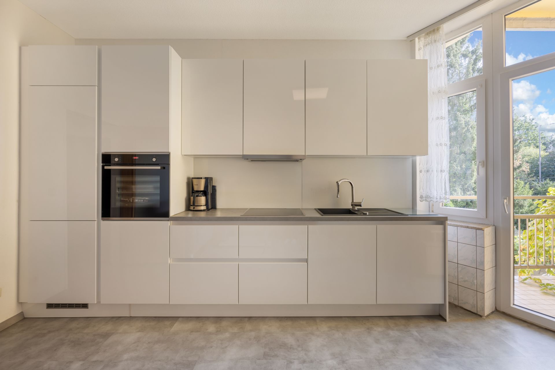 Moderne, helle Einbauküche mit weißen Schränken und großem Fenster zur Terrasse.