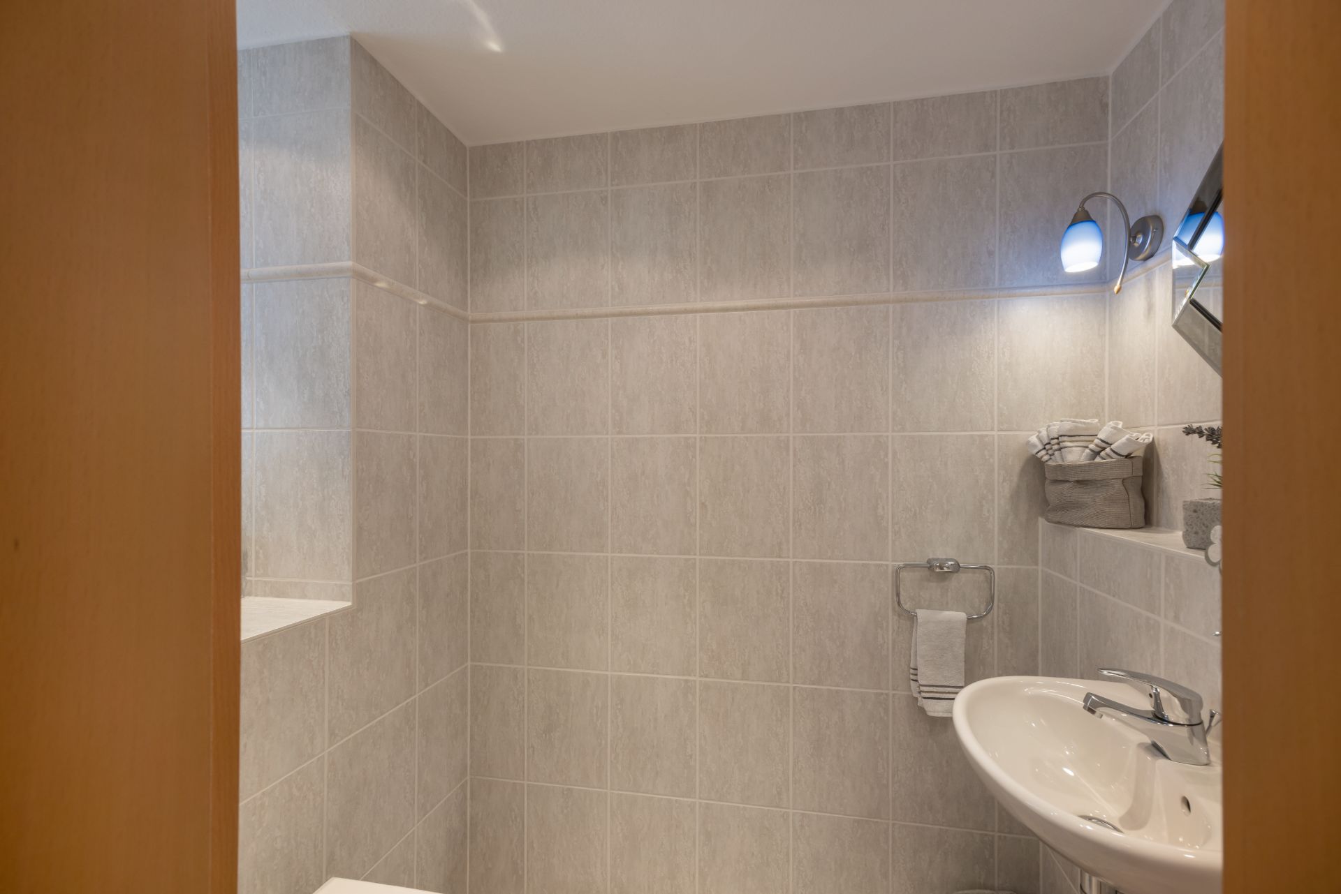 Kleines Badezimmer mit Waschbecken, Handtuchhalter und grauen Fliesen an den Wänden.