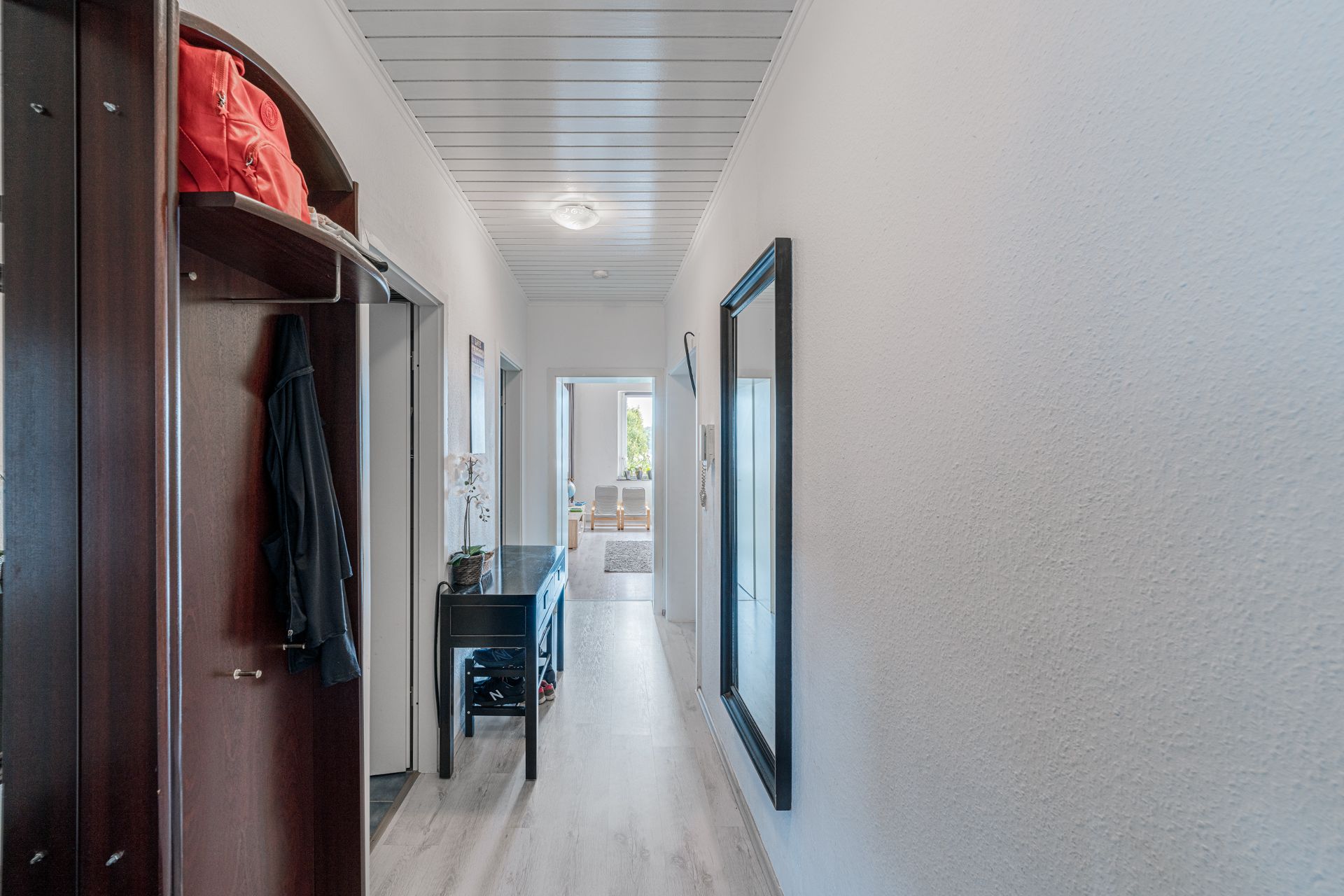 Heller Flur mit Garderobe, Spiegel und Blick in ein Wohnzimmer mit Fenster.