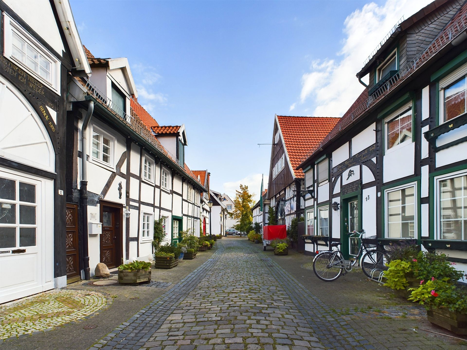 Gepflasterte Gasse mit Fachwerkhäusern und roten Ziegeldächern, einige Fahrräder an den Häusern.