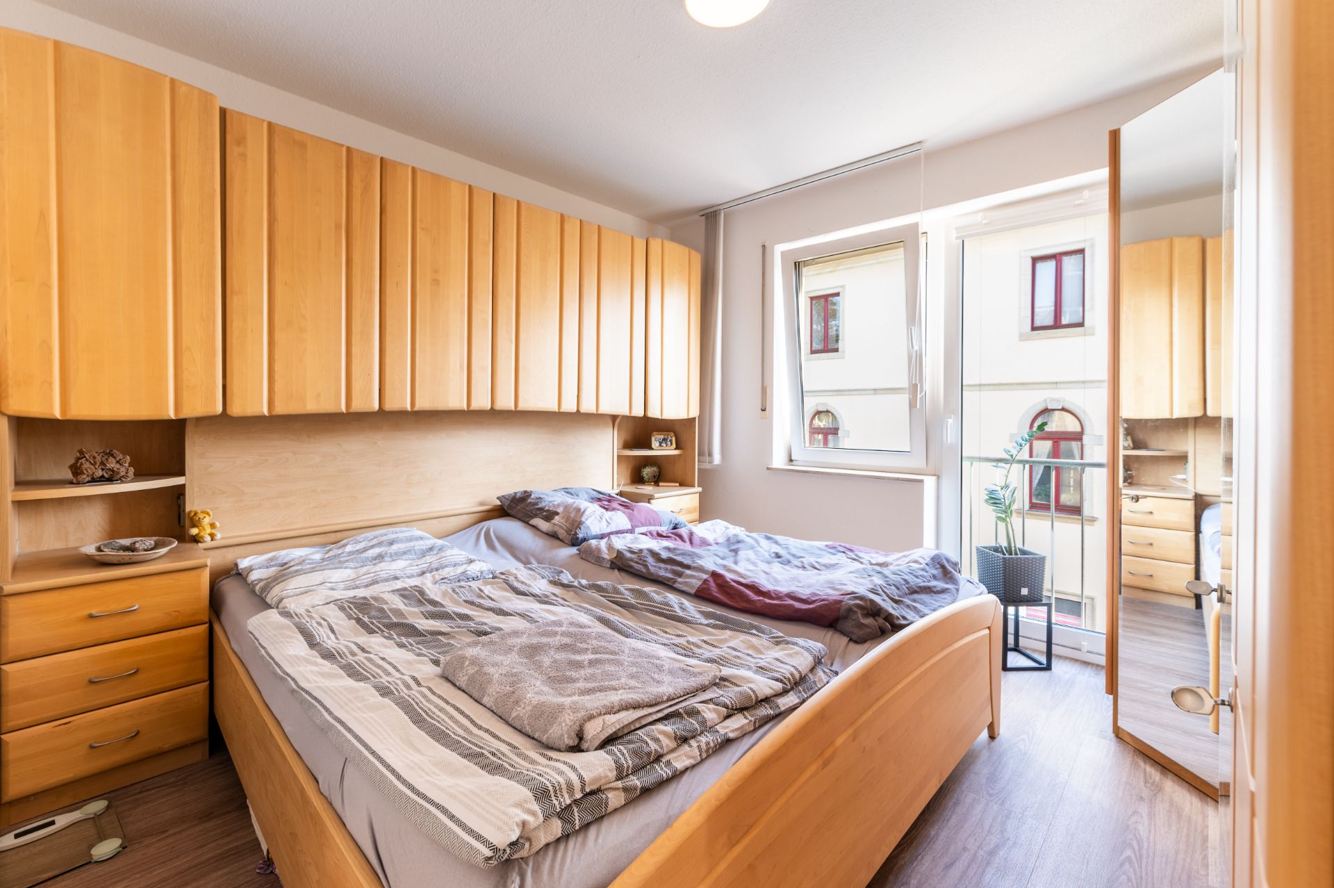Schlafzimmer mit Doppelbett, Holzschränken, Fenster und Spiegel an der Tür.
