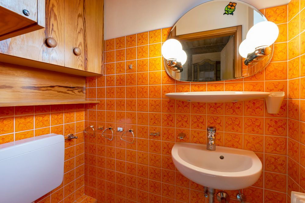 Kleines Bad mit orangefarbenen Fliesen, Waschbecken, Spiegel und Holzschränken.