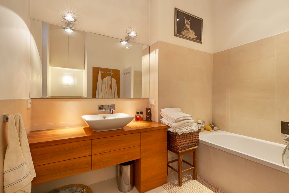 Modernes Badezimmer mit Holzwaschtisch, großem Spiegel und Badewanne, Handtücher auf Stuhl gestapelt.
