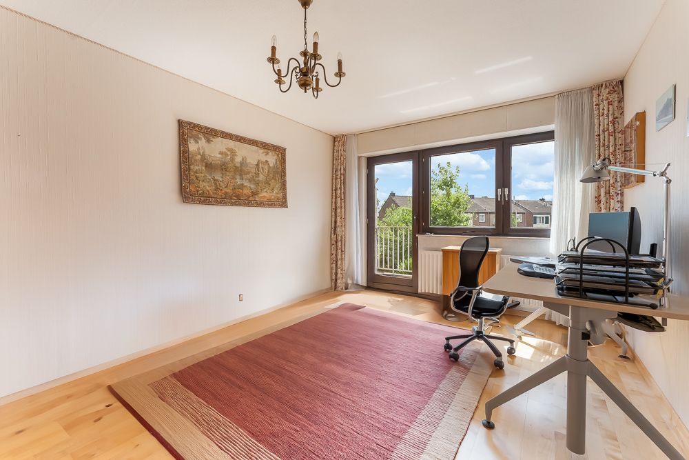 Helles Arbeitszimmer mit großem Teppich, Schreibtisch, Stuhl und Fenster mit Blick nach draußen.