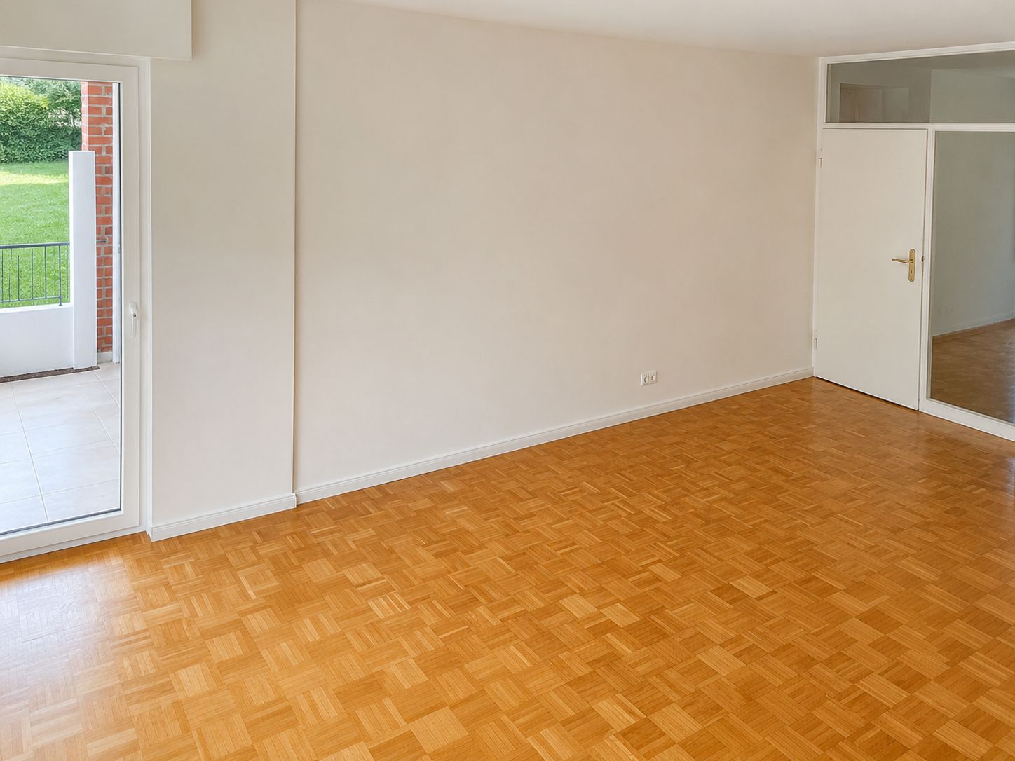 Leeres Zimmer mit Parkettboden, Glastür zum Garten und weißer Tür mit Fenster.