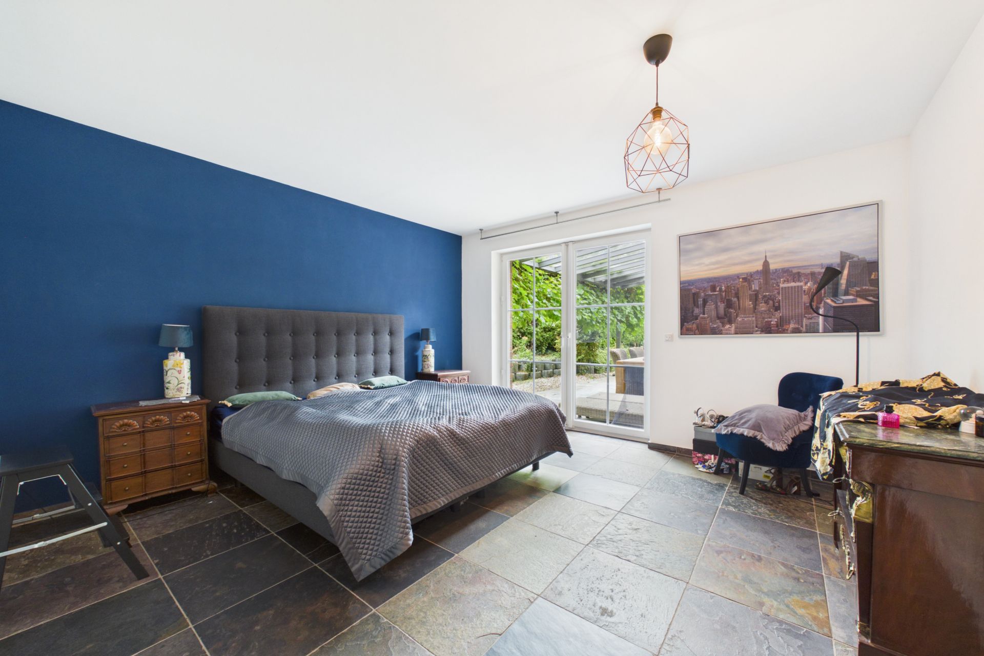 Schlafzimmer mit Doppelbett, blauer Wand, großem Fenster und Fliesenboden.
