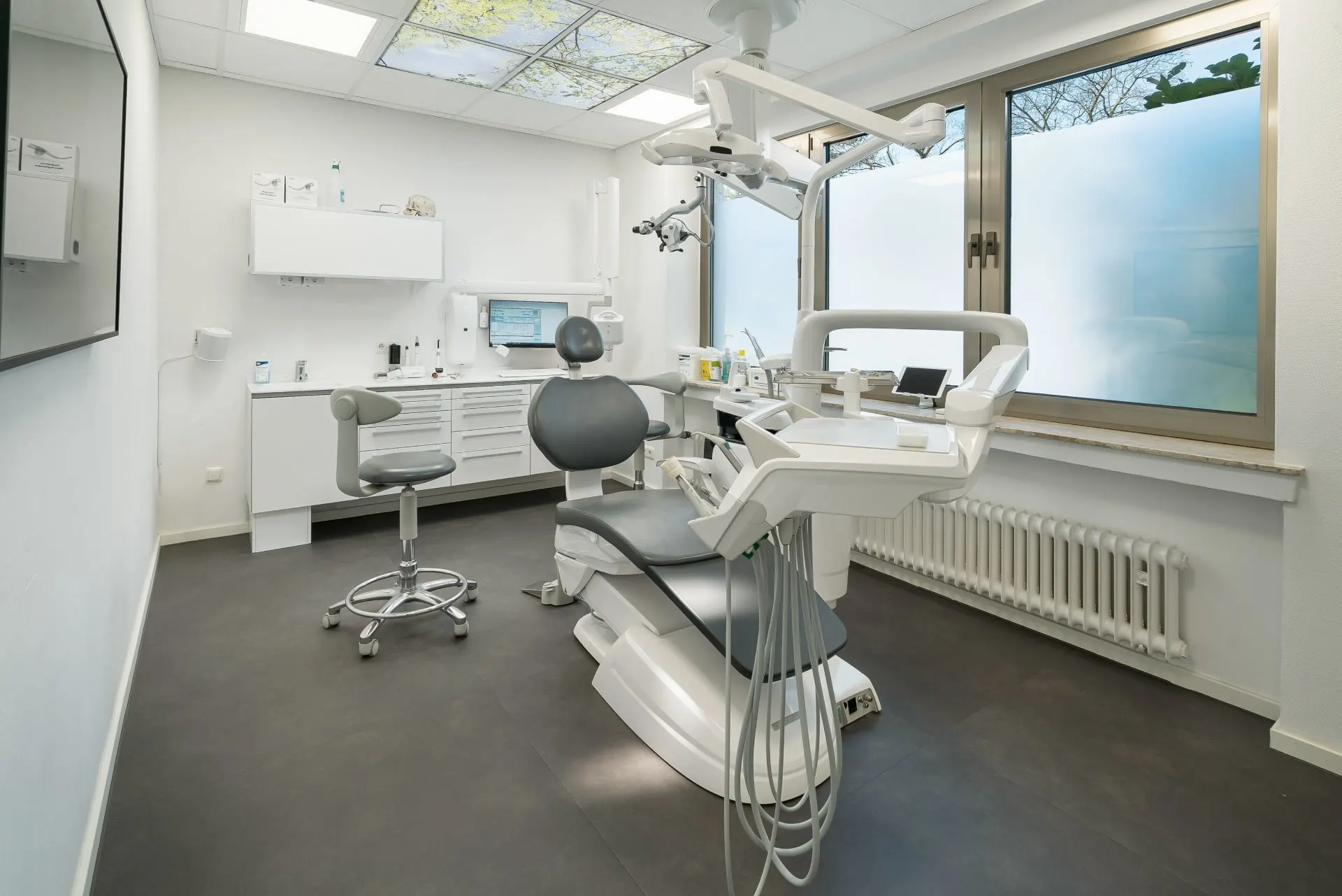 Ein heller Behandlungsraum mit einem Zahnarztstuhl und großem Fenster.