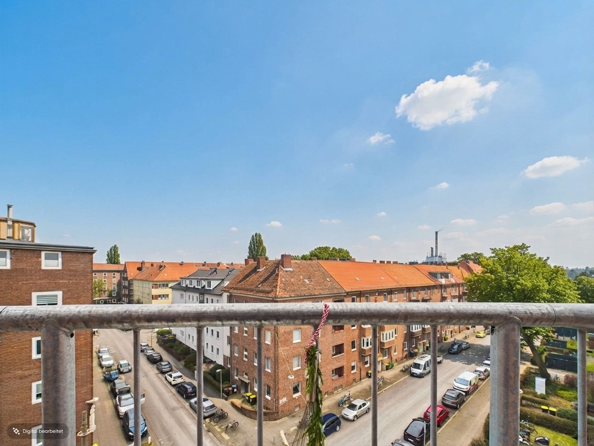Blick vom Balkon auf Wohngebäude mit roten Dächern und parkenden Autos bei sonnigem Wetter.
