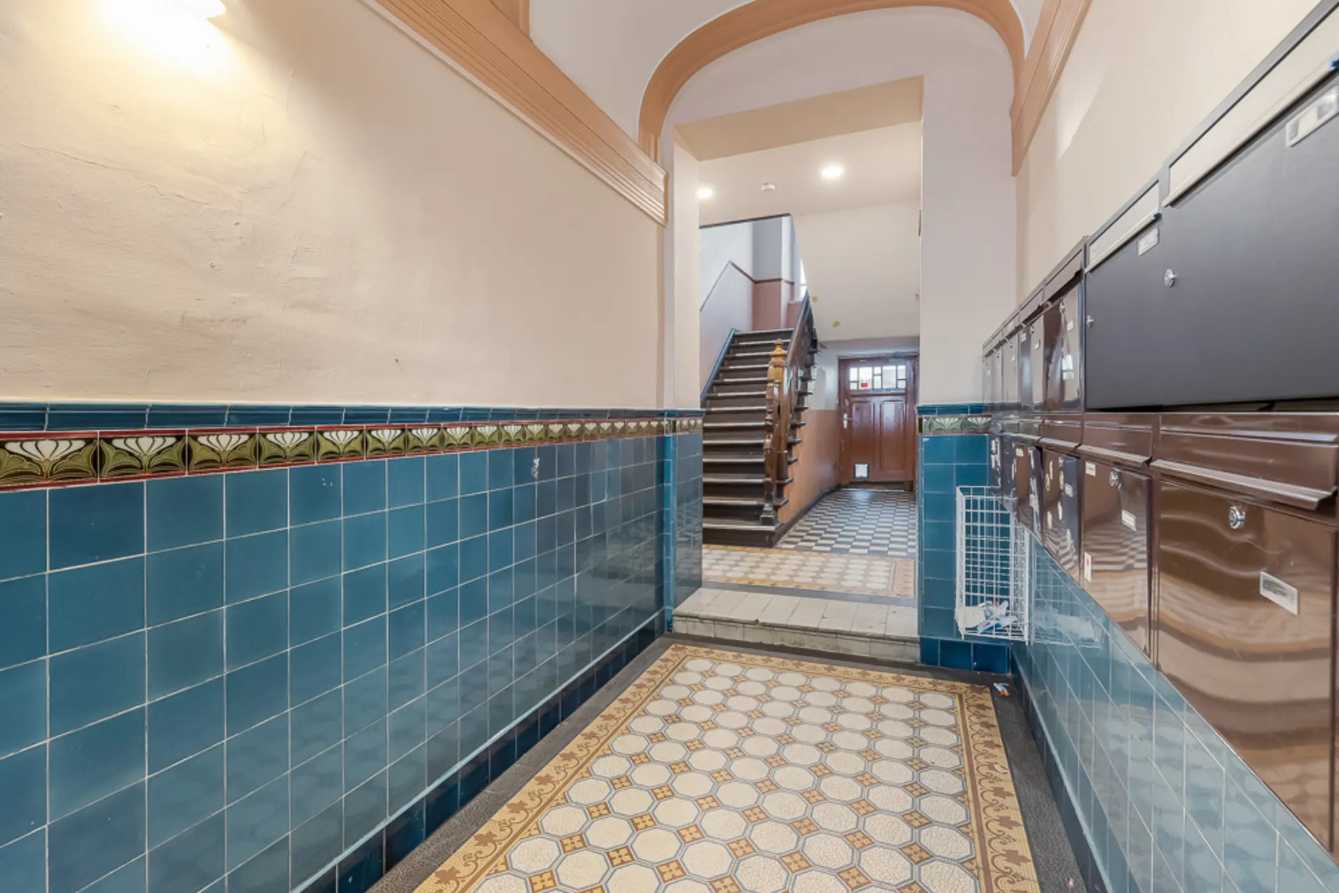 Eingangsbereich mit blauen Fliesen, Briefkästen und Treppe nach oben.
