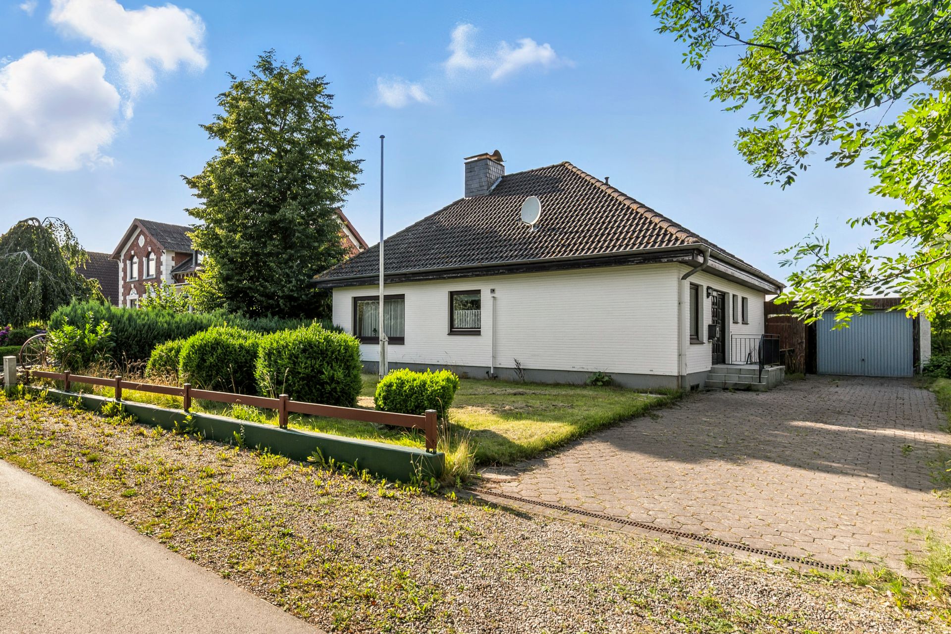 Ein einstöckiges weißes Haus mit Garten, Auffahrt und Garage an einem sonnigen Tag.