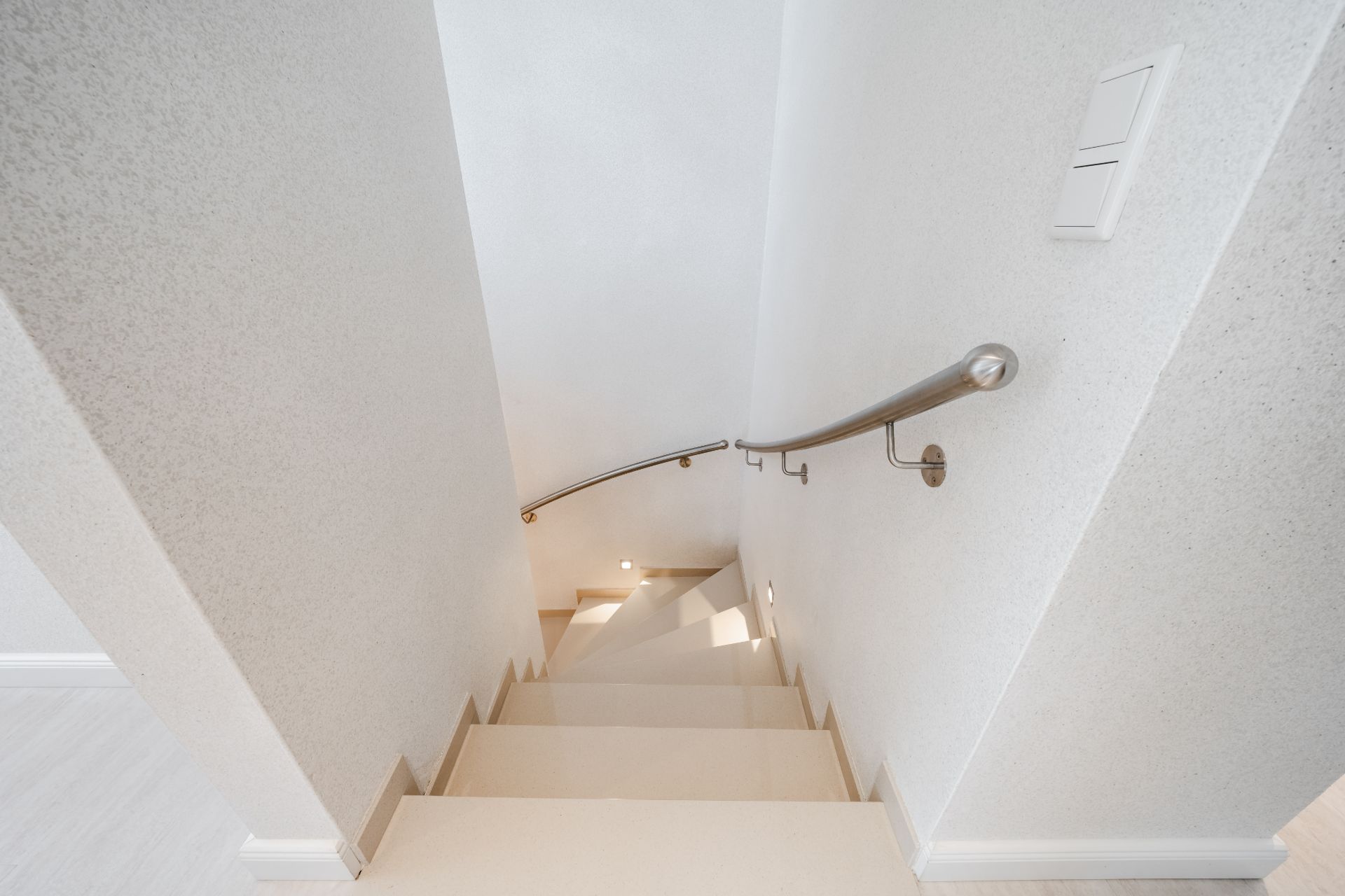 Helle Treppe mit Handlauf an weißer Wand, Blick von oben nach unten.