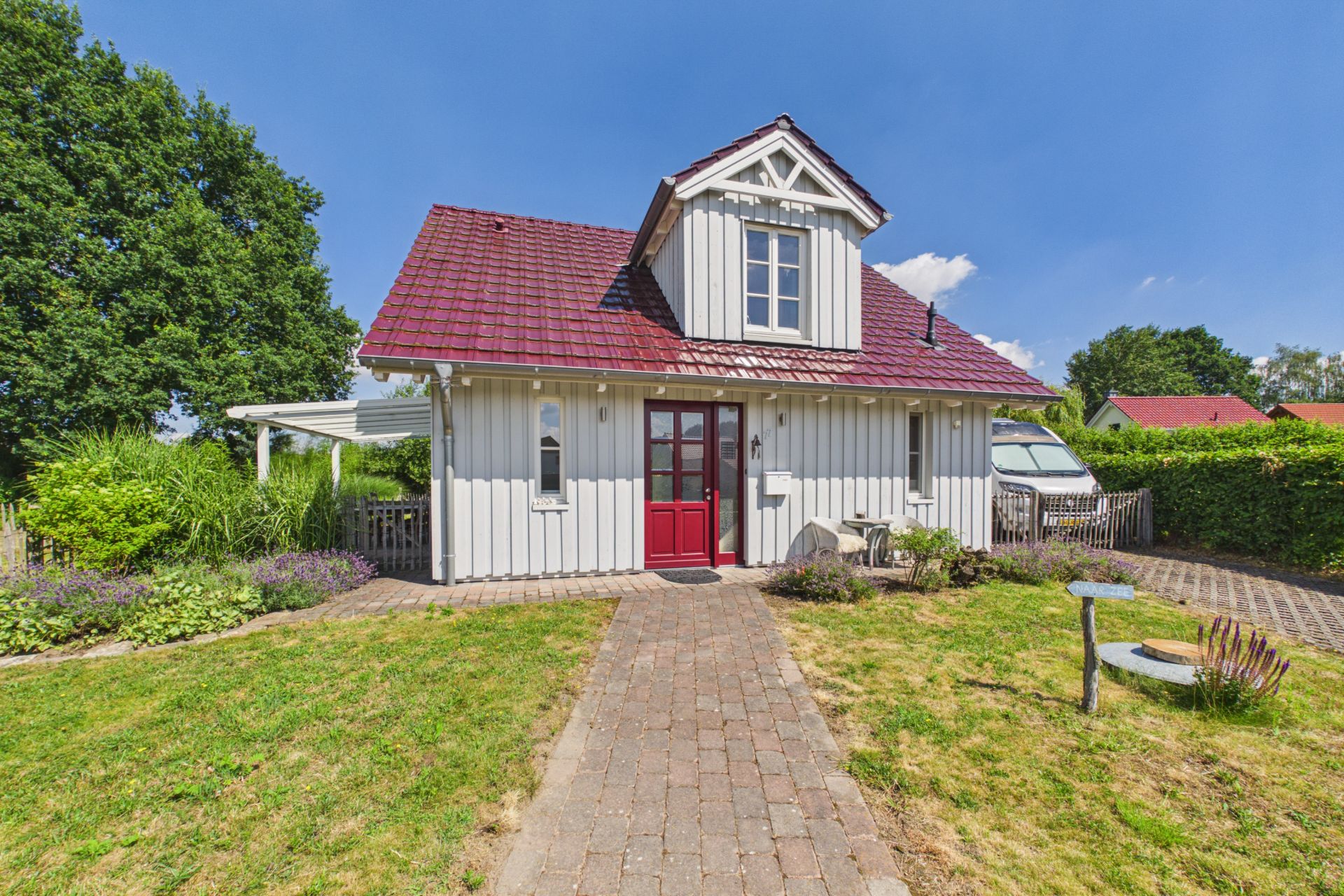 Weißes Einfamilienhaus mit rotem Dach, kleinem Garten und gepflastertem Weg zum Eingang.