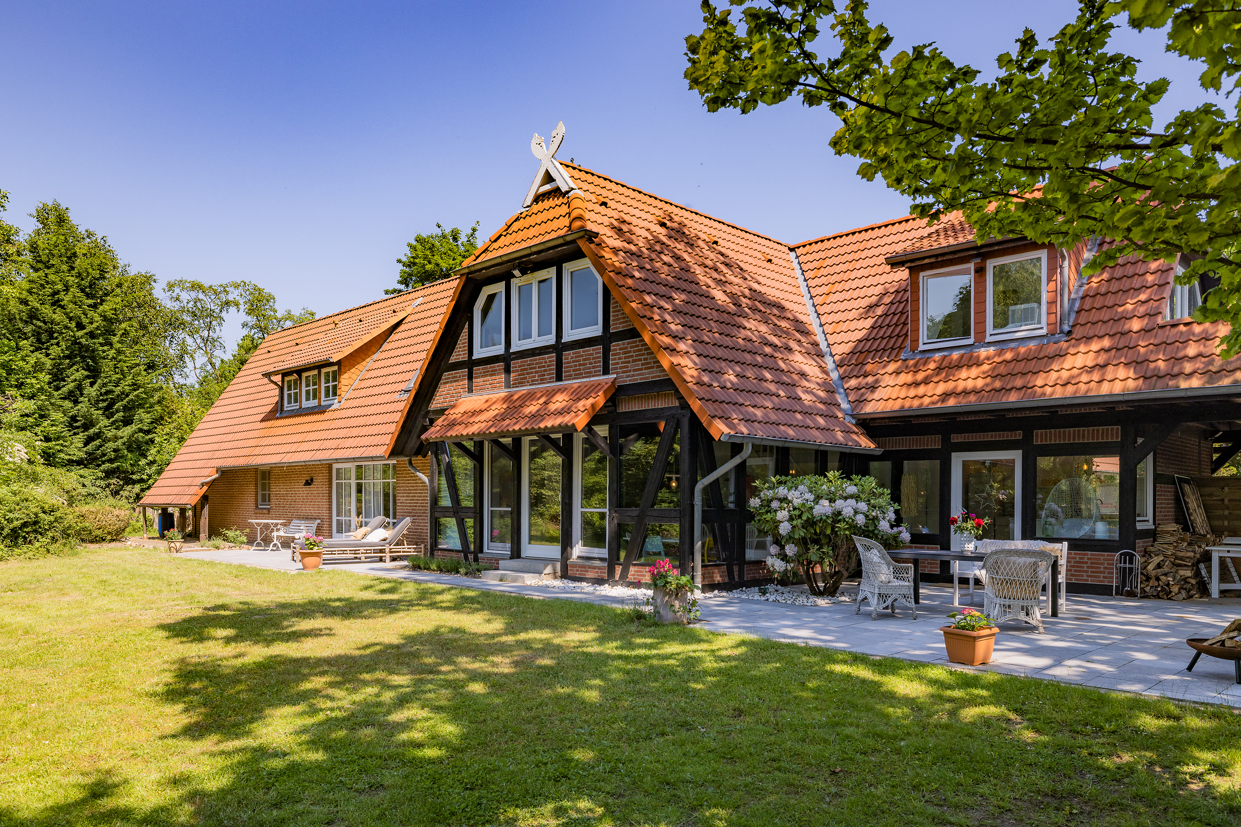 Backsteinwohnhaus mit rotem Ziegeldach, Terrasse und Garten im Grünen.