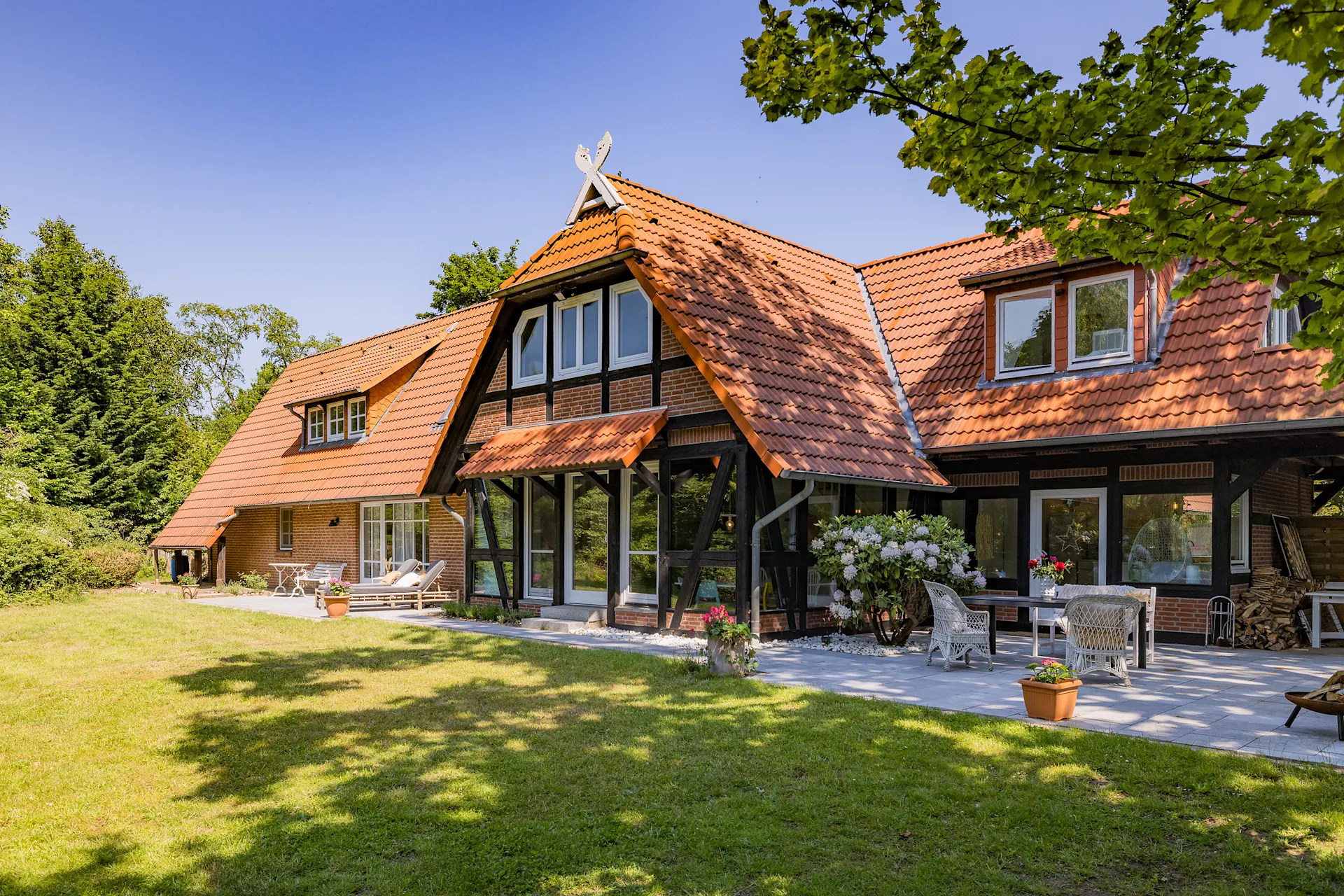 Backsteinwohnhaus mit rotem Ziegeldach, Terrasse und Garten im Grünen.