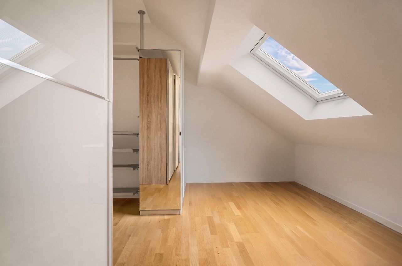 Helles Zimmer mit Dachschräge, Holzfußboden und großem Dachfenster.