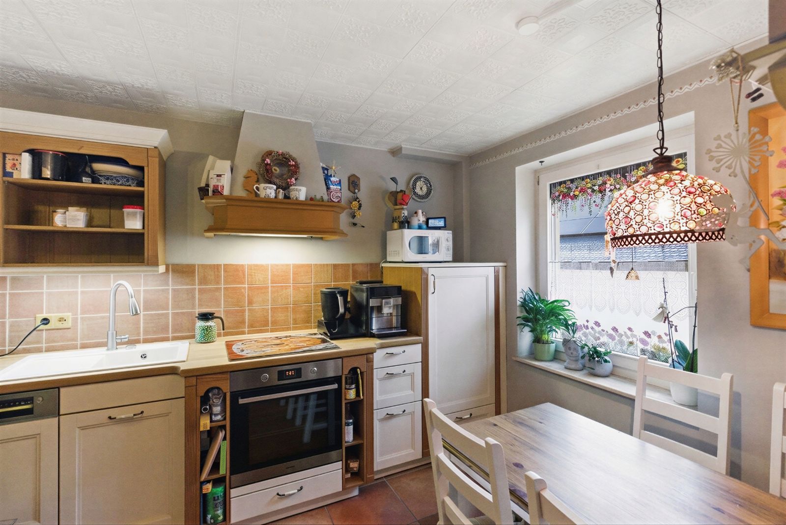Gemütliche Küche mit Esstisch, Holzschränken, Herd, Spüle und Fensterbank mit Pflanzen.
