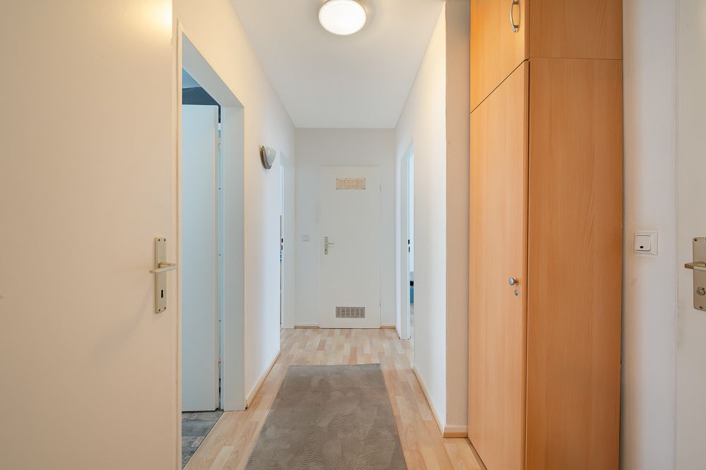 Heller Flur mit Holzboden, Teppichläufer und Einbauschrank an der rechten Wand.