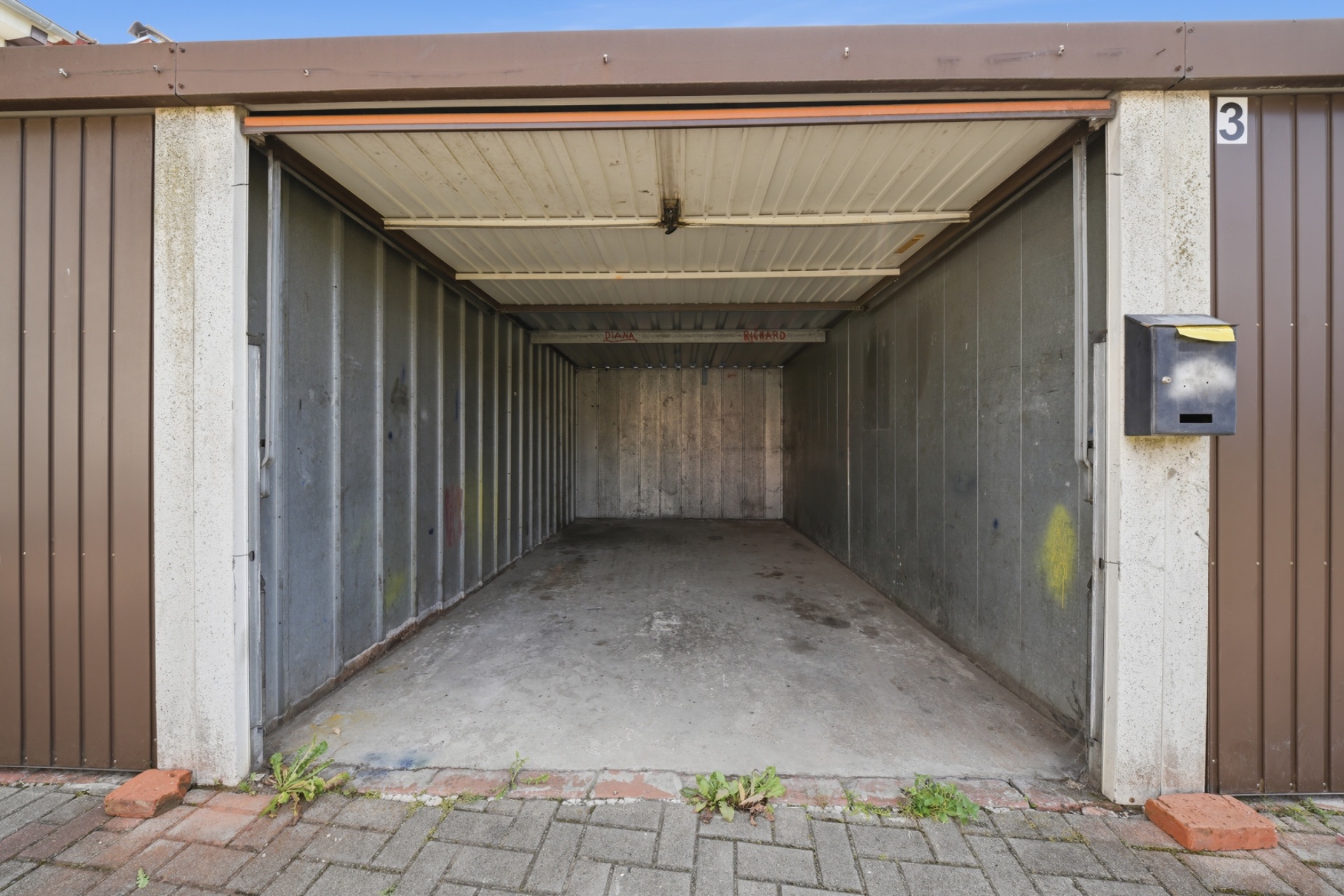 Leere Garage mit offenem Tor und gepflastertem Boden davor.