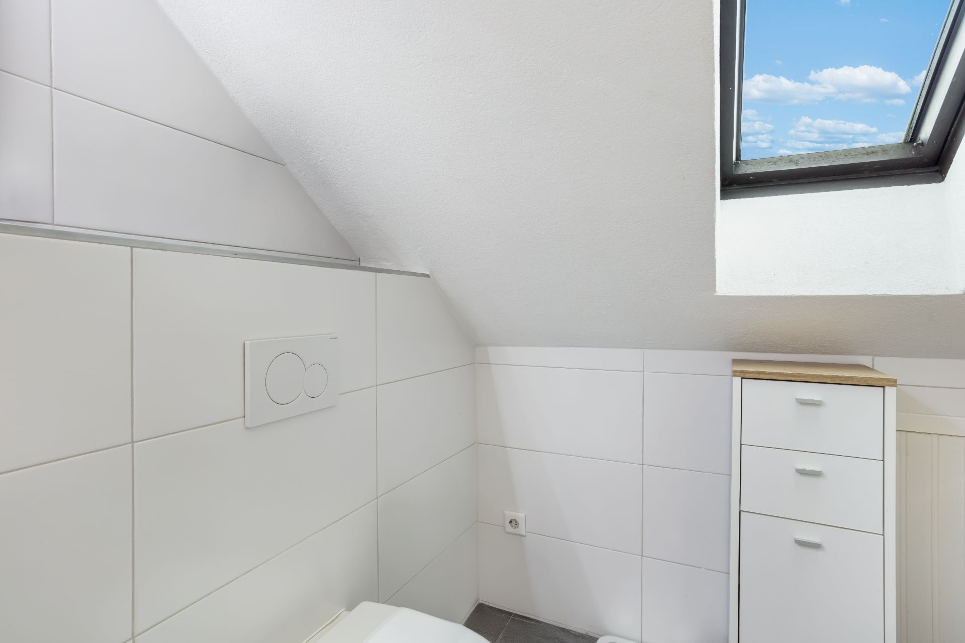Helles Badezimmer mit weißem Fliesenspiegel, Dachfenster und weißem Schrank.