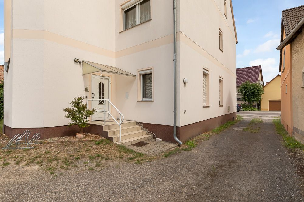 Eingang eines hellen Wohnhauses mit Treppe und kleinem Vordach, daneben ein Fahrradständer.