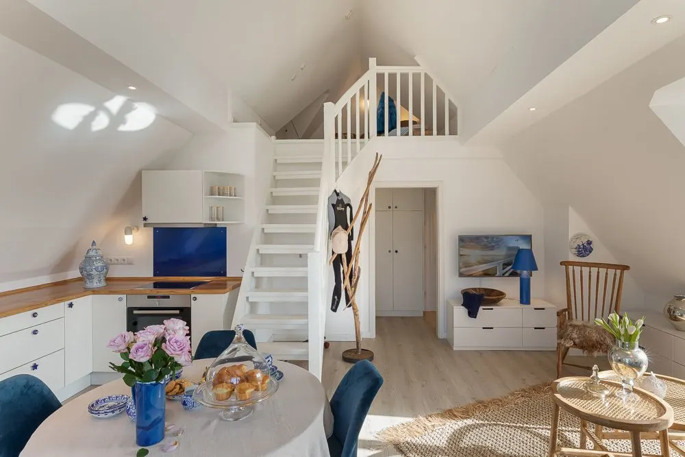 Helles Wohnzimmer mit Küchenzeile, Esstisch und Treppe zur offenen Galerie.