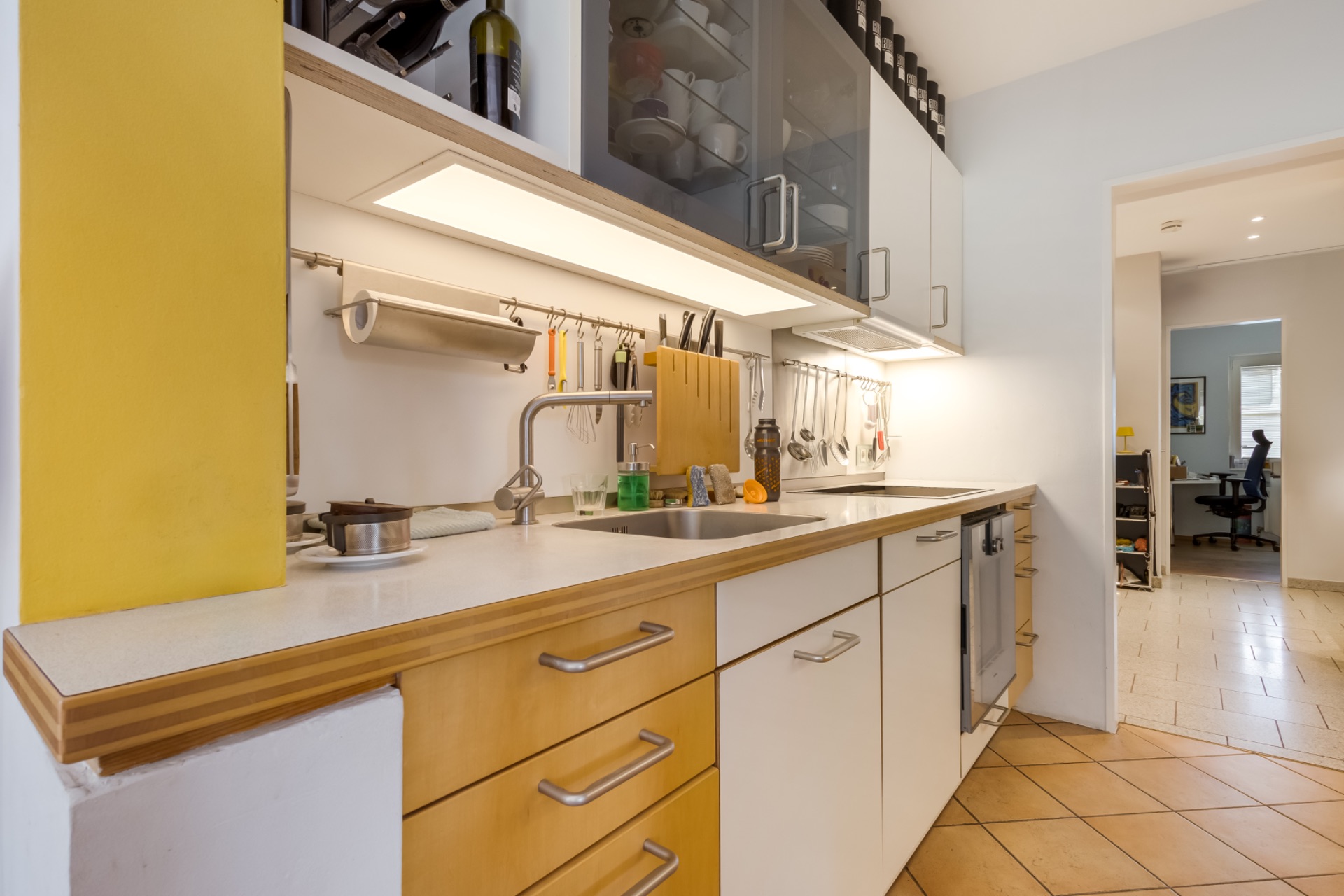 Moderne Küche mit Holzmöbeln, Spüle und Geräten, Blick ins angrenzende Arbeitszimmer.