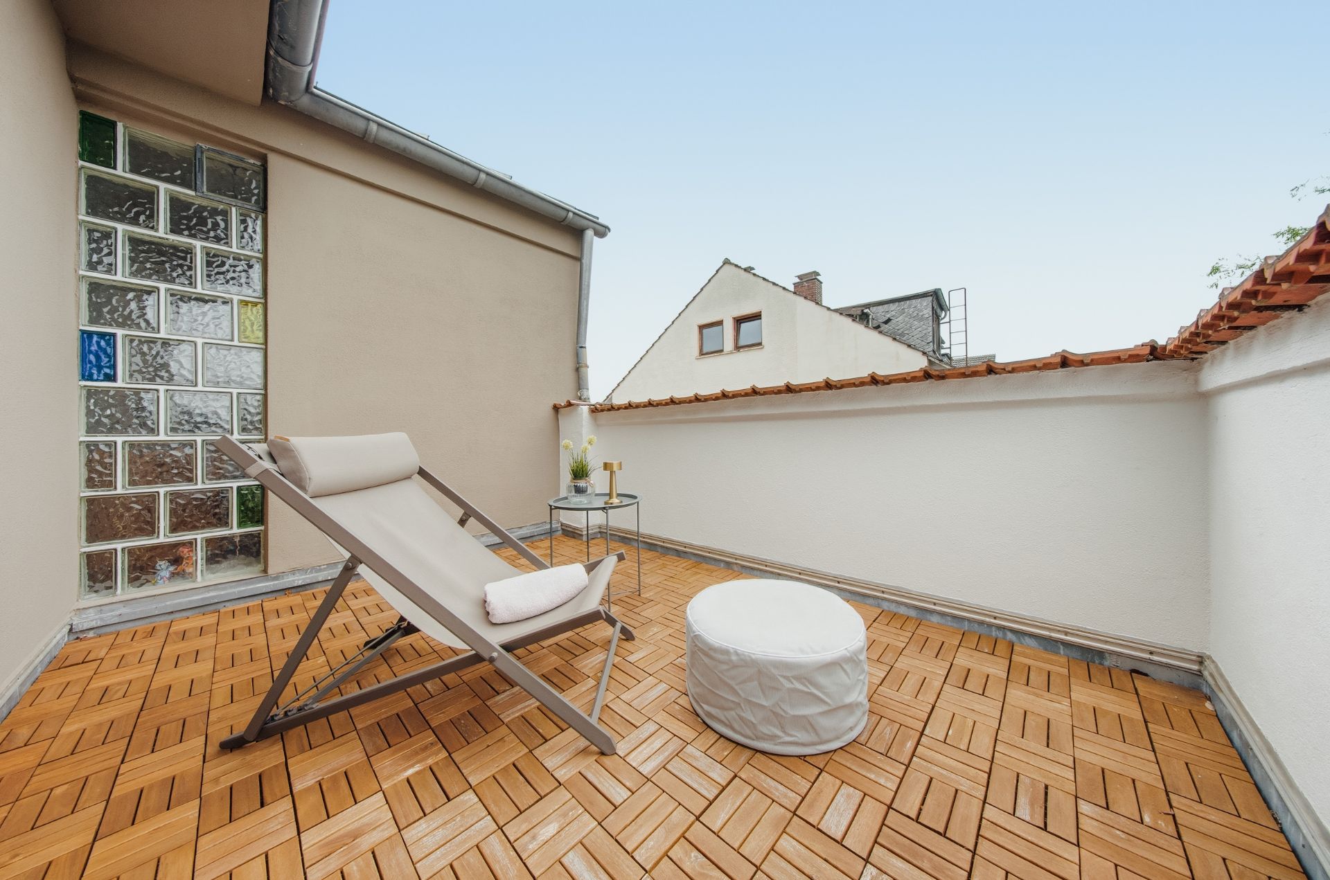 Kleine Dachterrasse mit Liegestuhl, rundem Hocker und Holzboden.