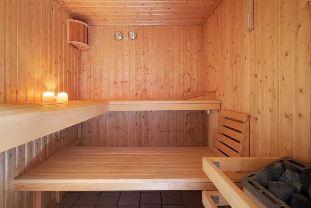 Holzsauna mit zwei Bänken, Saunaofen, zwei Kerzen und Wandthermometern.