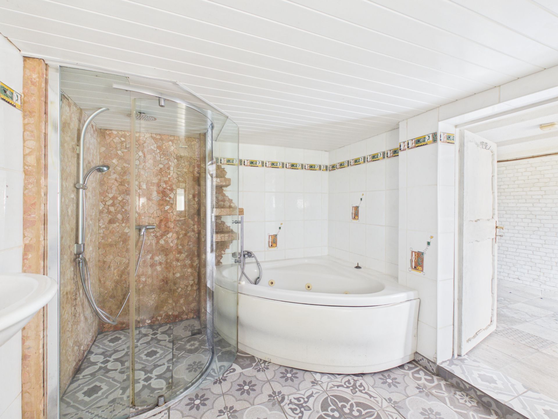 Helles Bad mit Eckbadewanne, Dusche mit Glastür und buntem Fliesenboden.