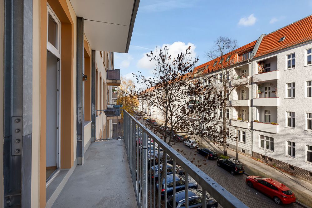 Balkon mit Blick auf eine ruhige Wohnstraße mit parkenden Autos und Bäumen.