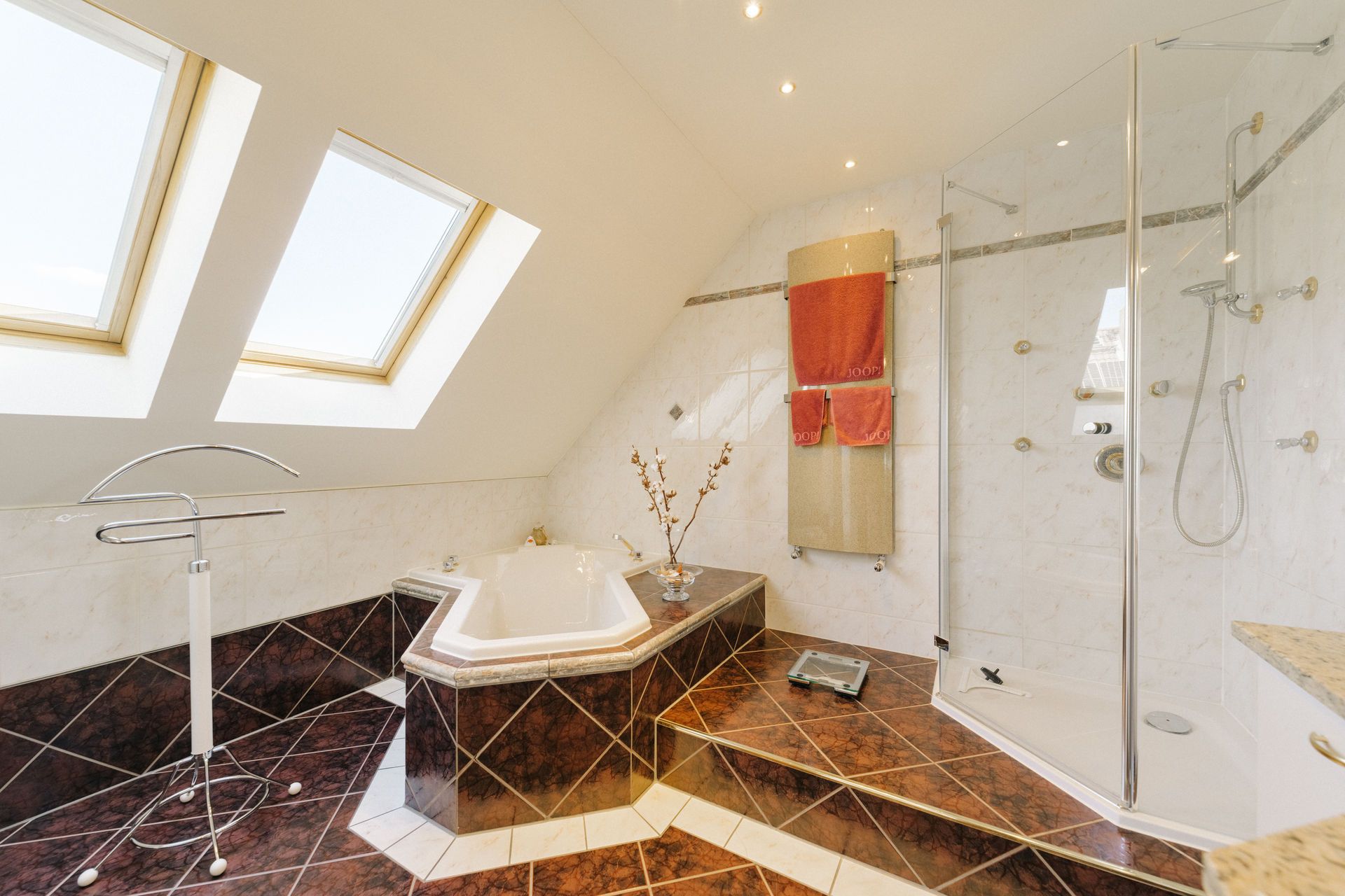 Helles Badezimmer mit Eckbadewanne, Dusche, zwei Dachfenstern und dunklen Fliesen.