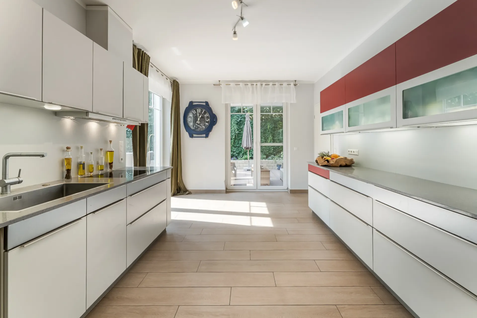 Moderne, helle Küche mit weißen Schränken, Holzfußboden und großer Glastür zum Garten.