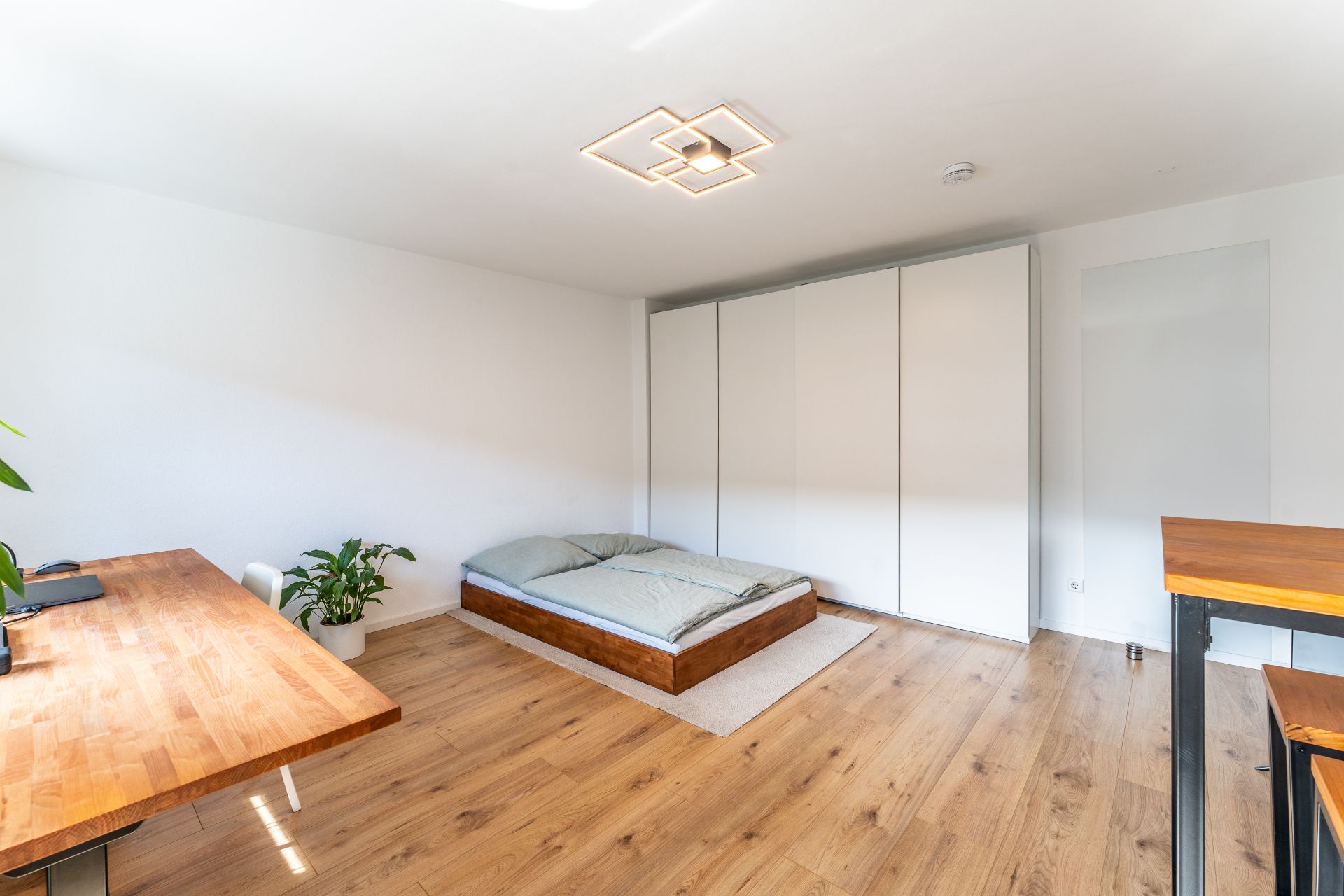 Modernes Schlafzimmer mit Holzfußboden, niedrigem Bett, großem Kleiderschrank und Schreibtisch.