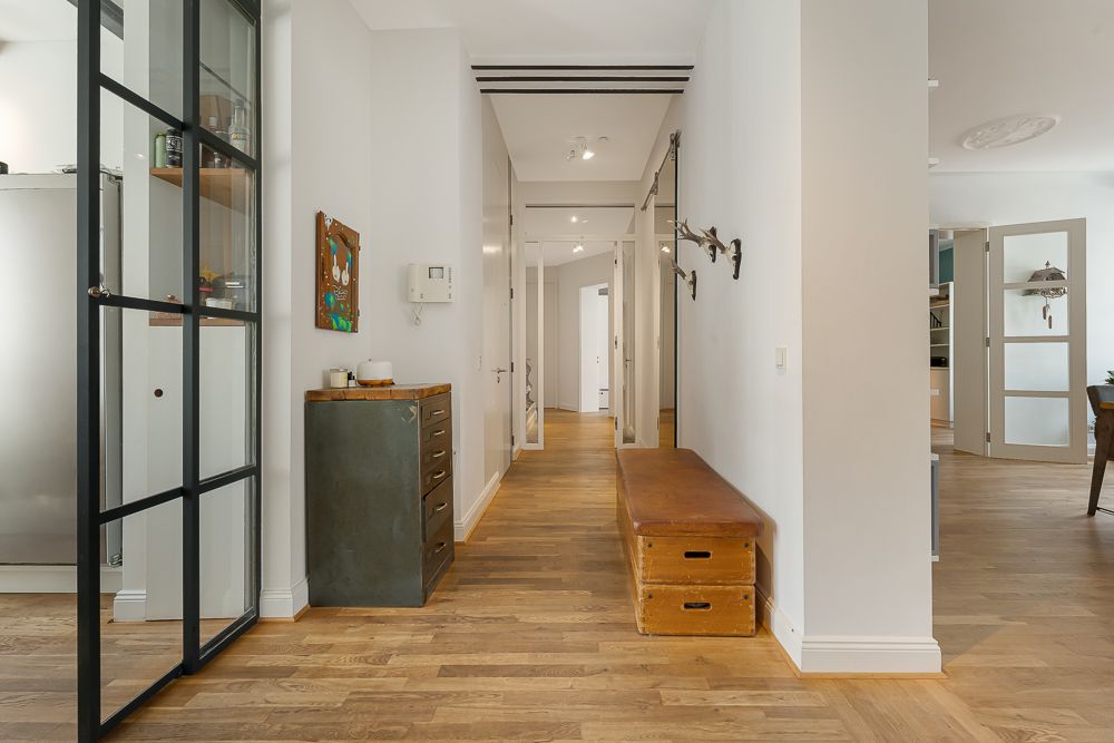 Heller Flur mit Holzboden, Bank, Kommode und Wandhaken in einer Wohnung.