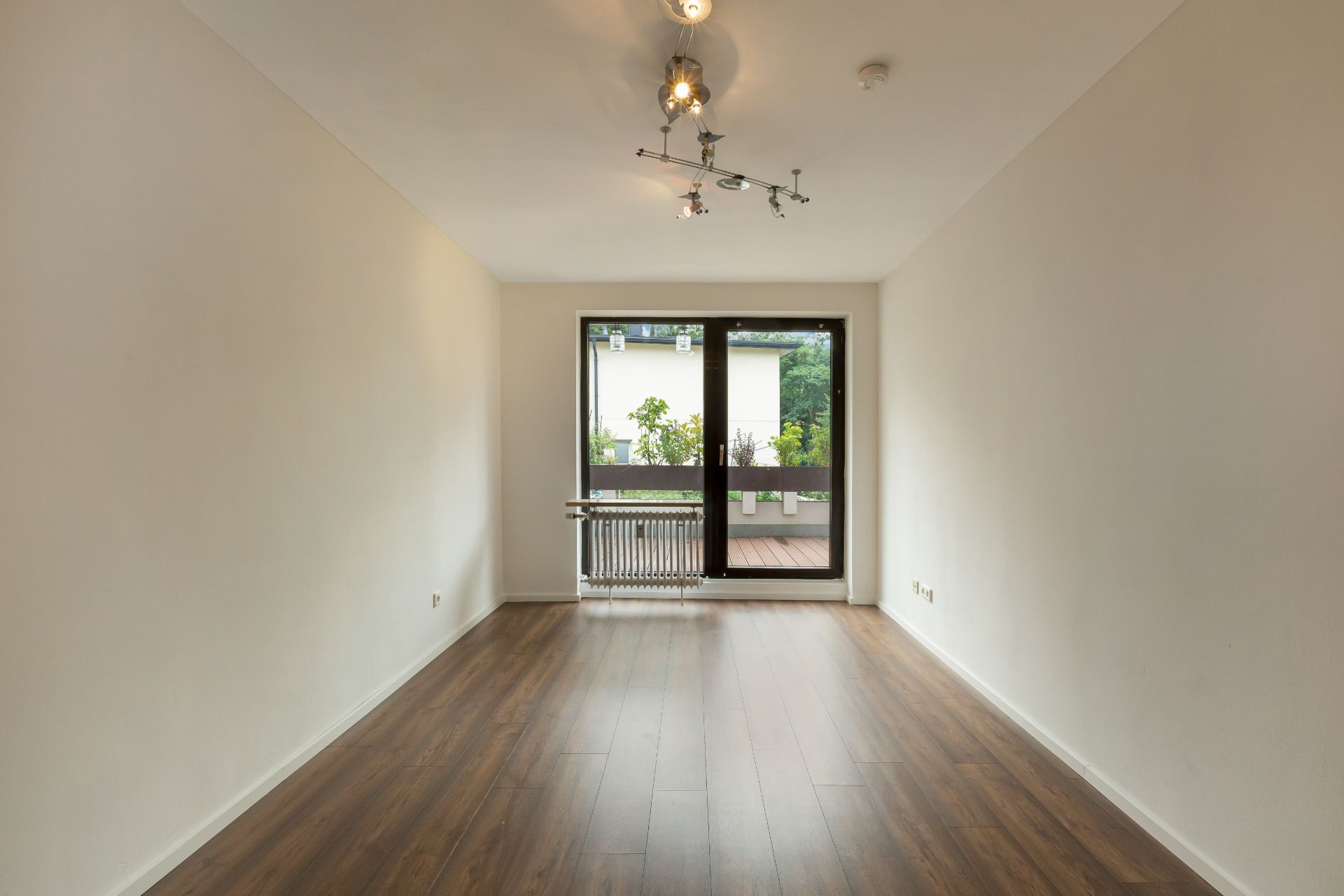 Leerer Raum mit Holzboden, weißen Wänden und Fenster mit Blick auf Balkon.