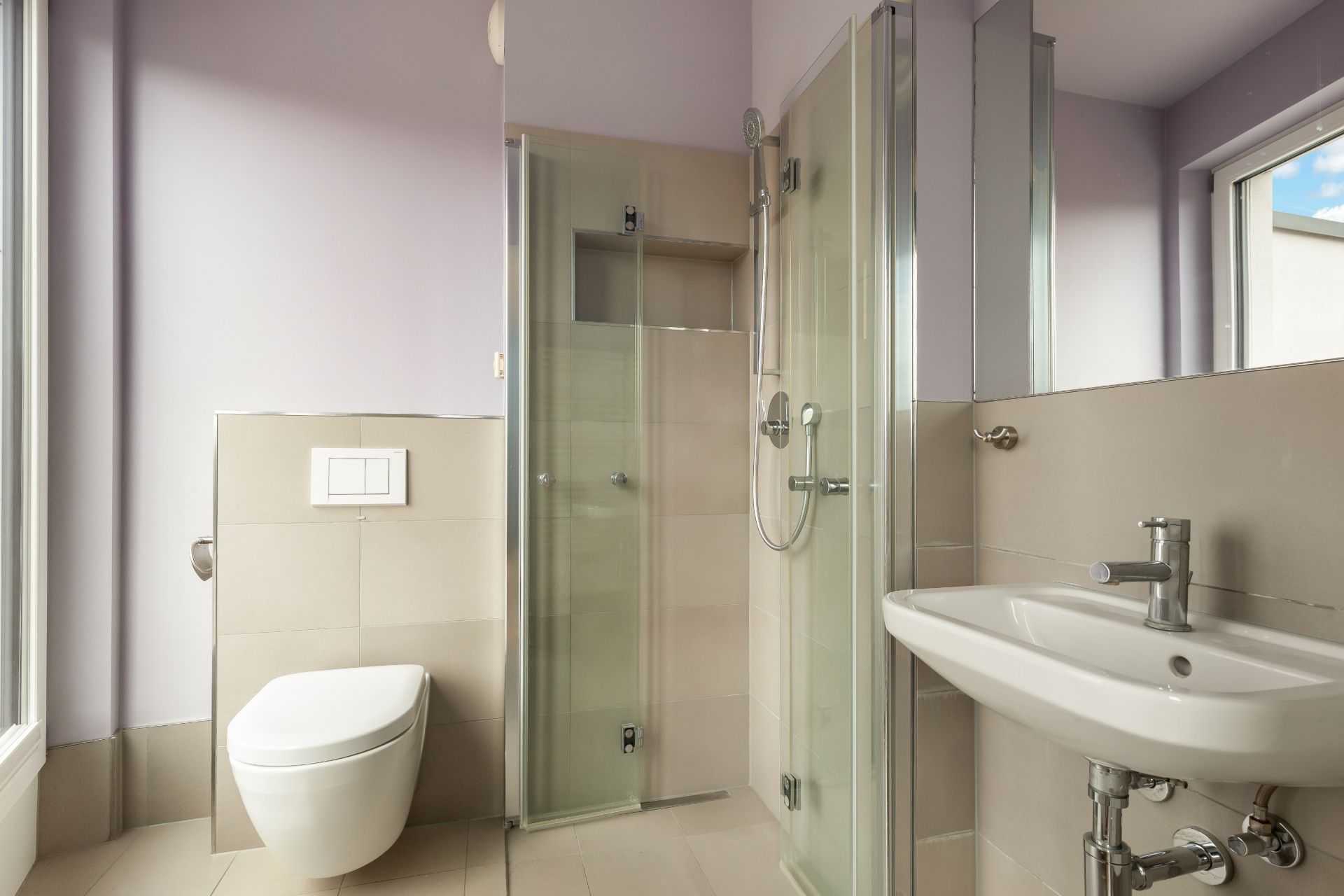 Modernes Badezimmer mit Toilette, Dusche und Waschbecken, große Fenster sorgen für Tageslicht.