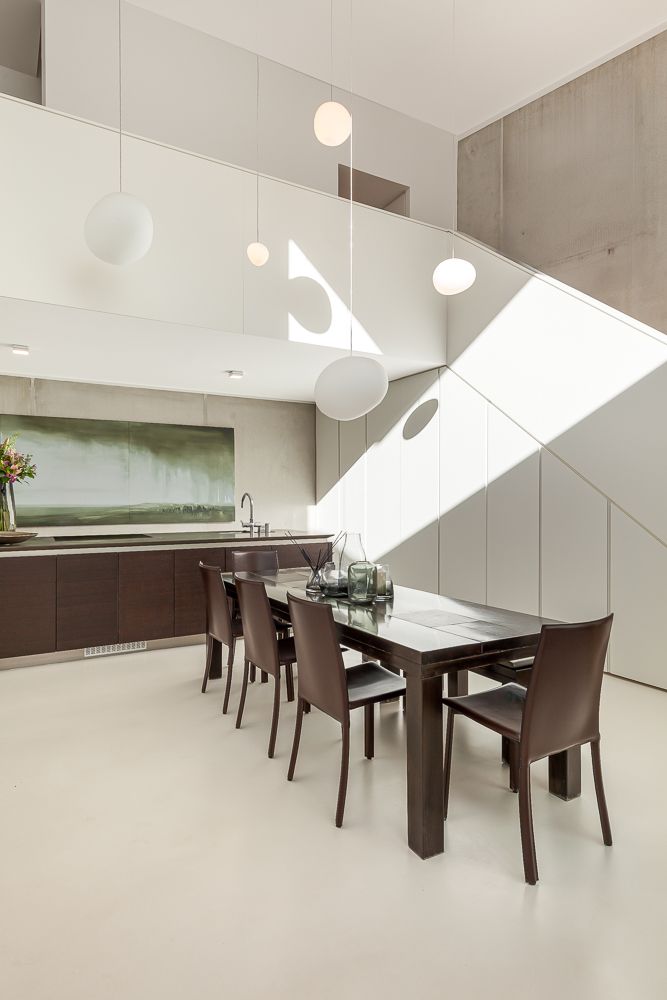 Helle Küche mit Holztisch, sechs Stühlen, Hängelampen und moderner Treppe im Hintergrund.