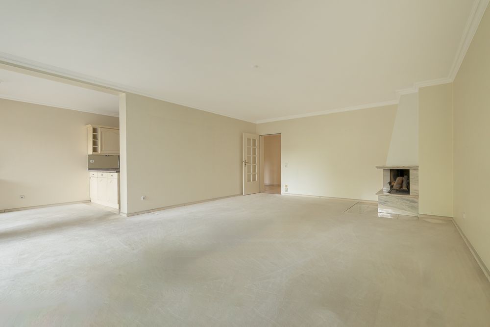 Leeres Wohnzimmer mit offenem Zugang zur Küche und Kamin in der Ecke.