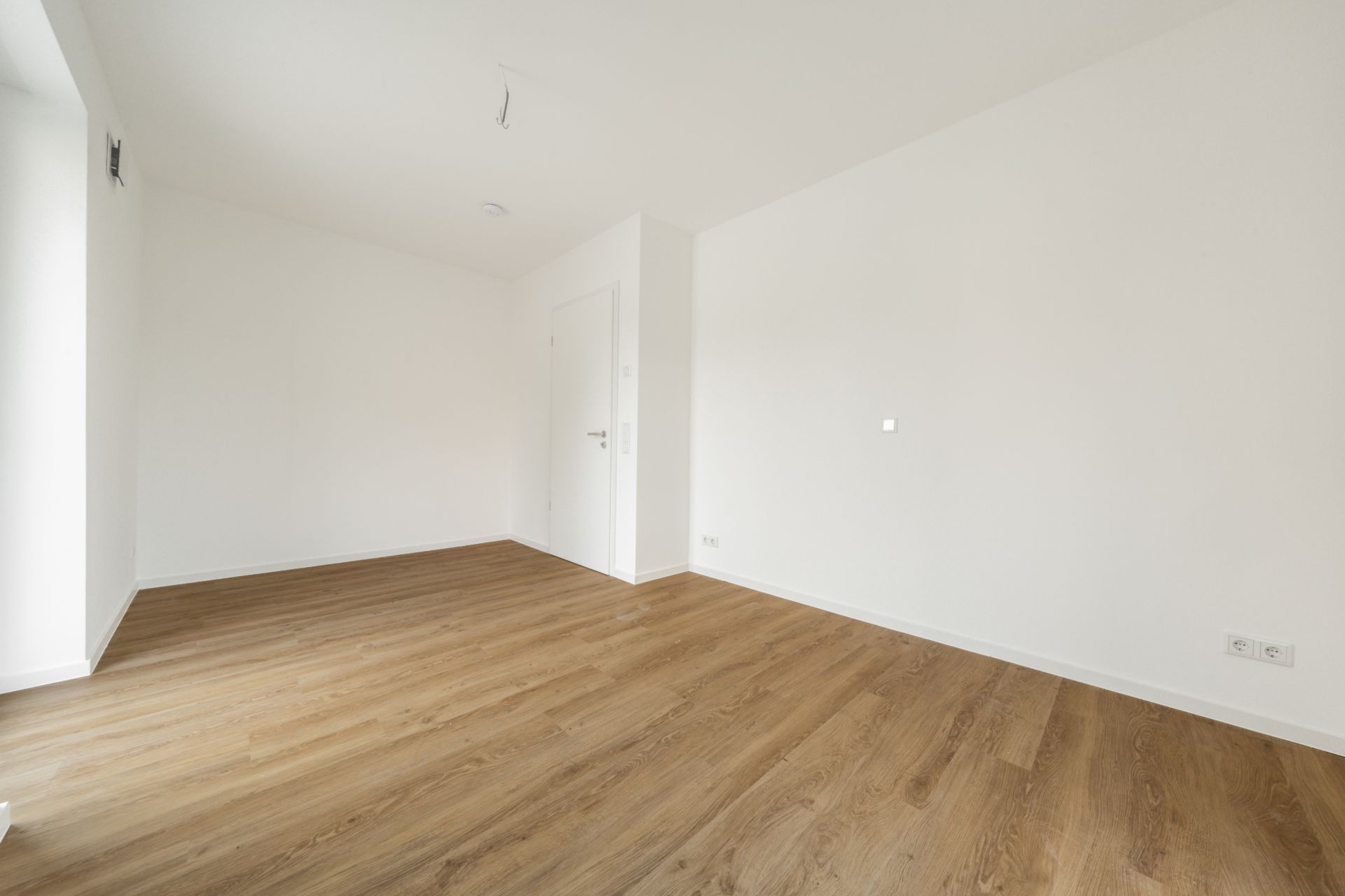 Leerer Raum mit weiß gestrichenen Wänden und hellem Holzfußboden.