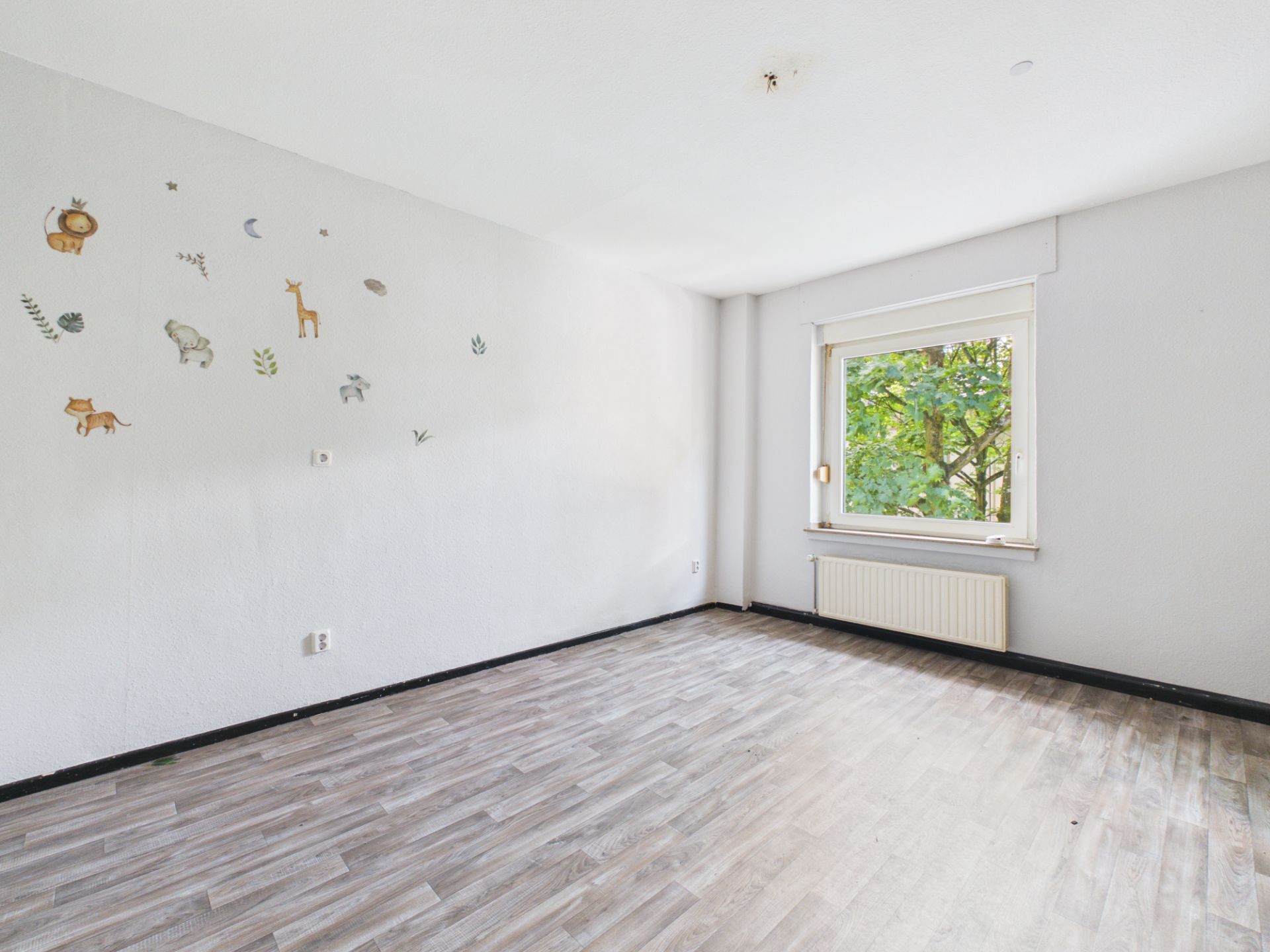 Leeres Zimmer mit Fenster, hellem Boden und Wandstickern mit Tieren.