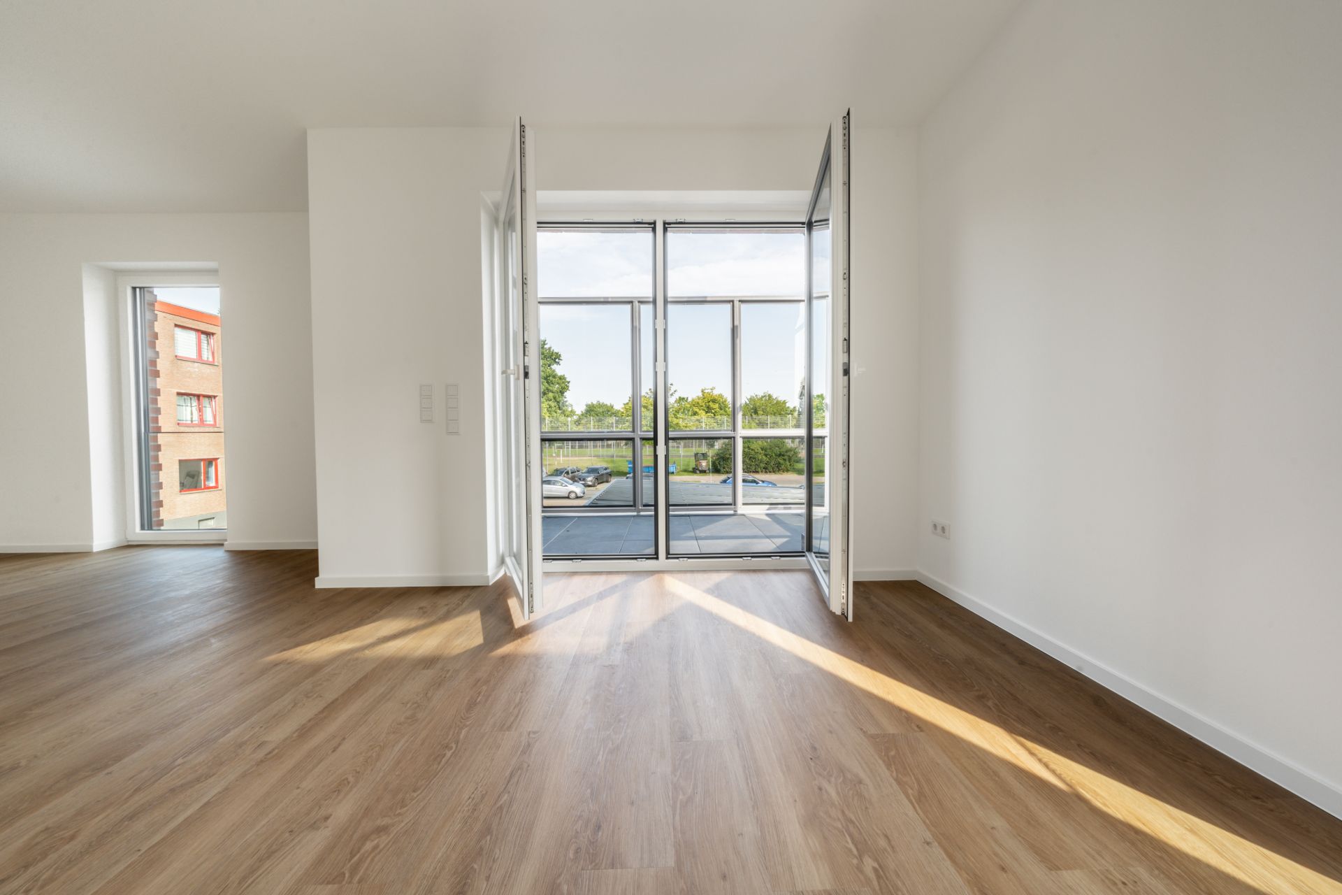 Heller Raum mit Parkettboden und großen Flügeltüren zu einem Balkon.